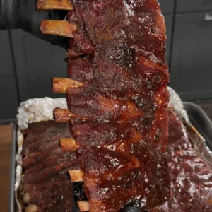 Glazed smoked pork ribs being held up showing caramelized bark and exposed bones