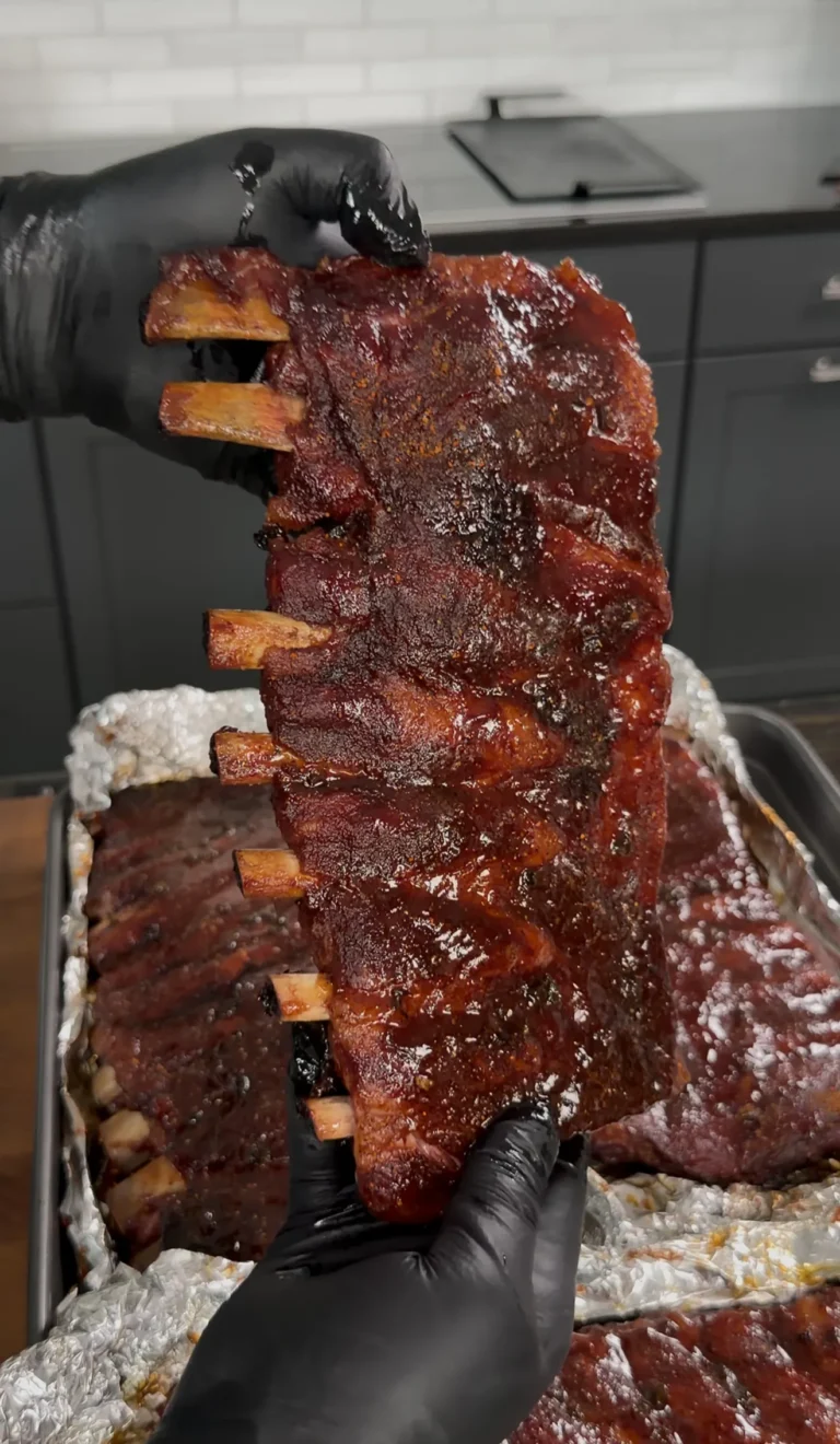 Glazed smoked pork ribs being held up showing caramelized bark and exposed bones
