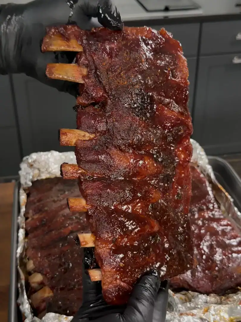 Glazed smoked pork ribs being held up showing caramelized bark and exposed bones
