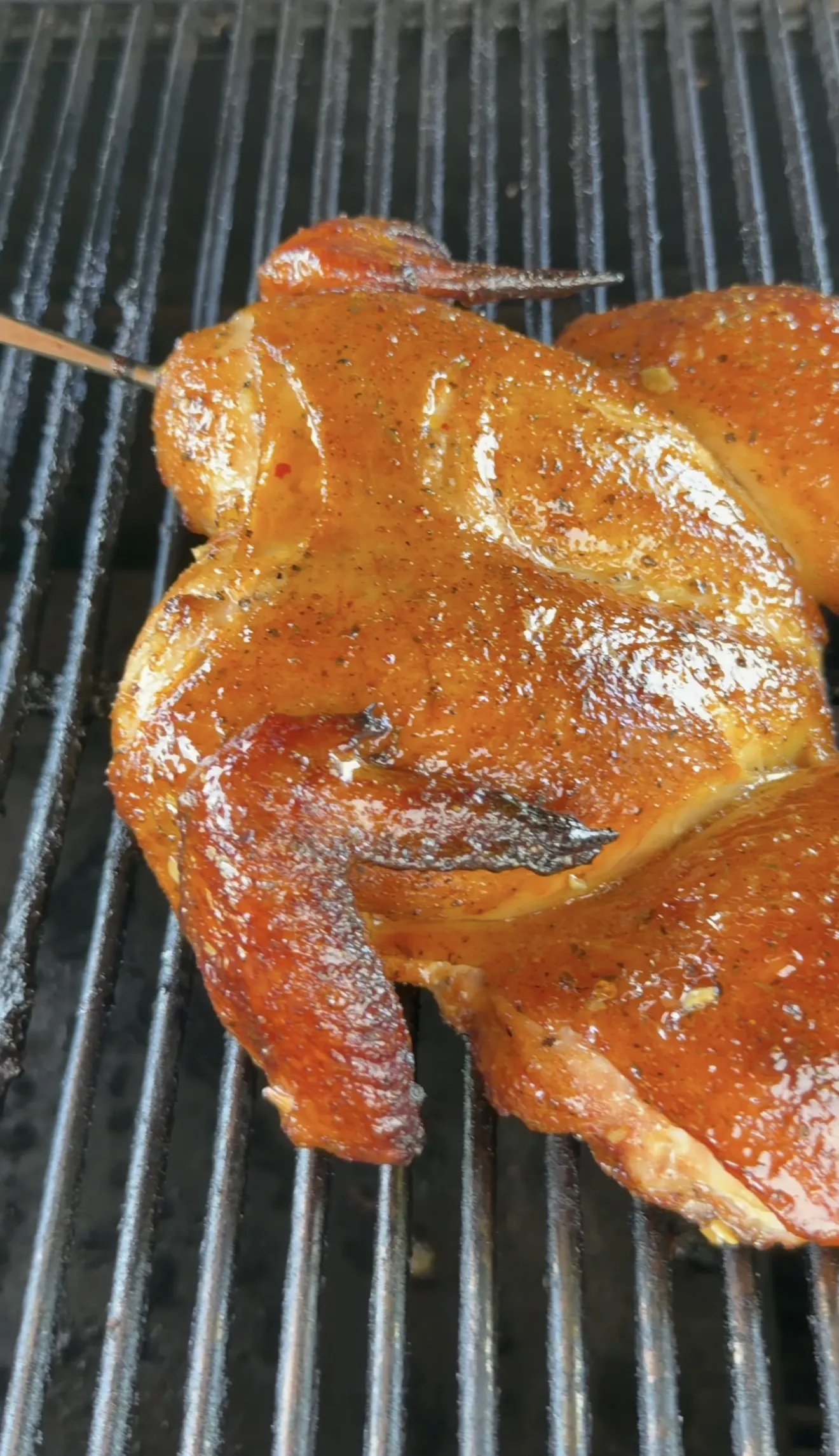 Golden brown spatchcock chicken with crispy skin on grill grates after temperature bump