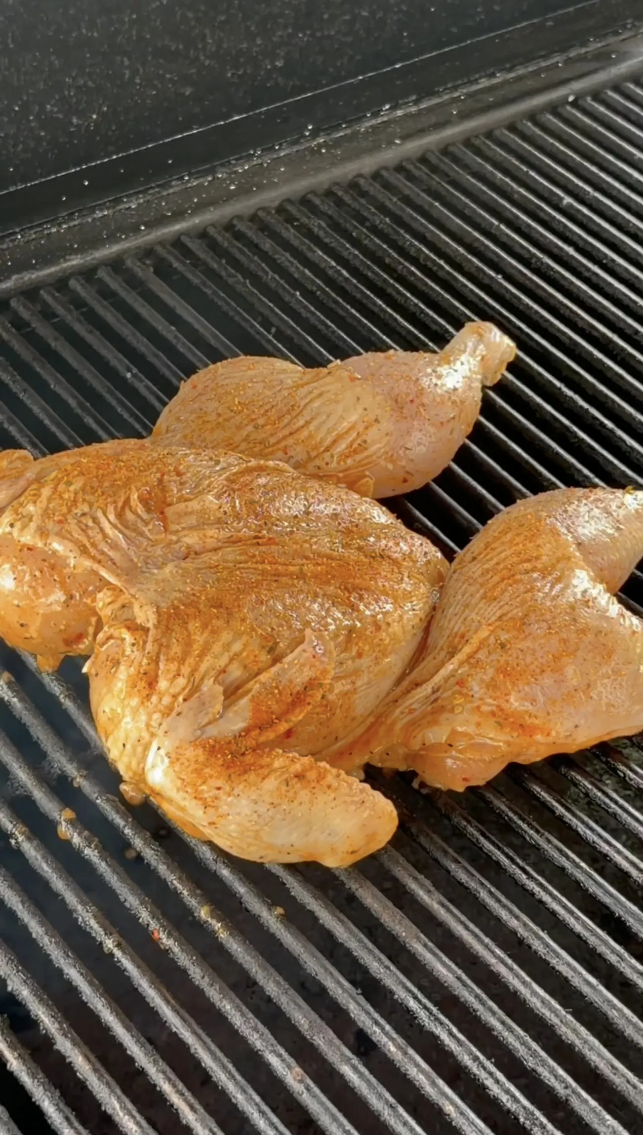 Spatchcock chicken cooking on grill grates during the smoke phase