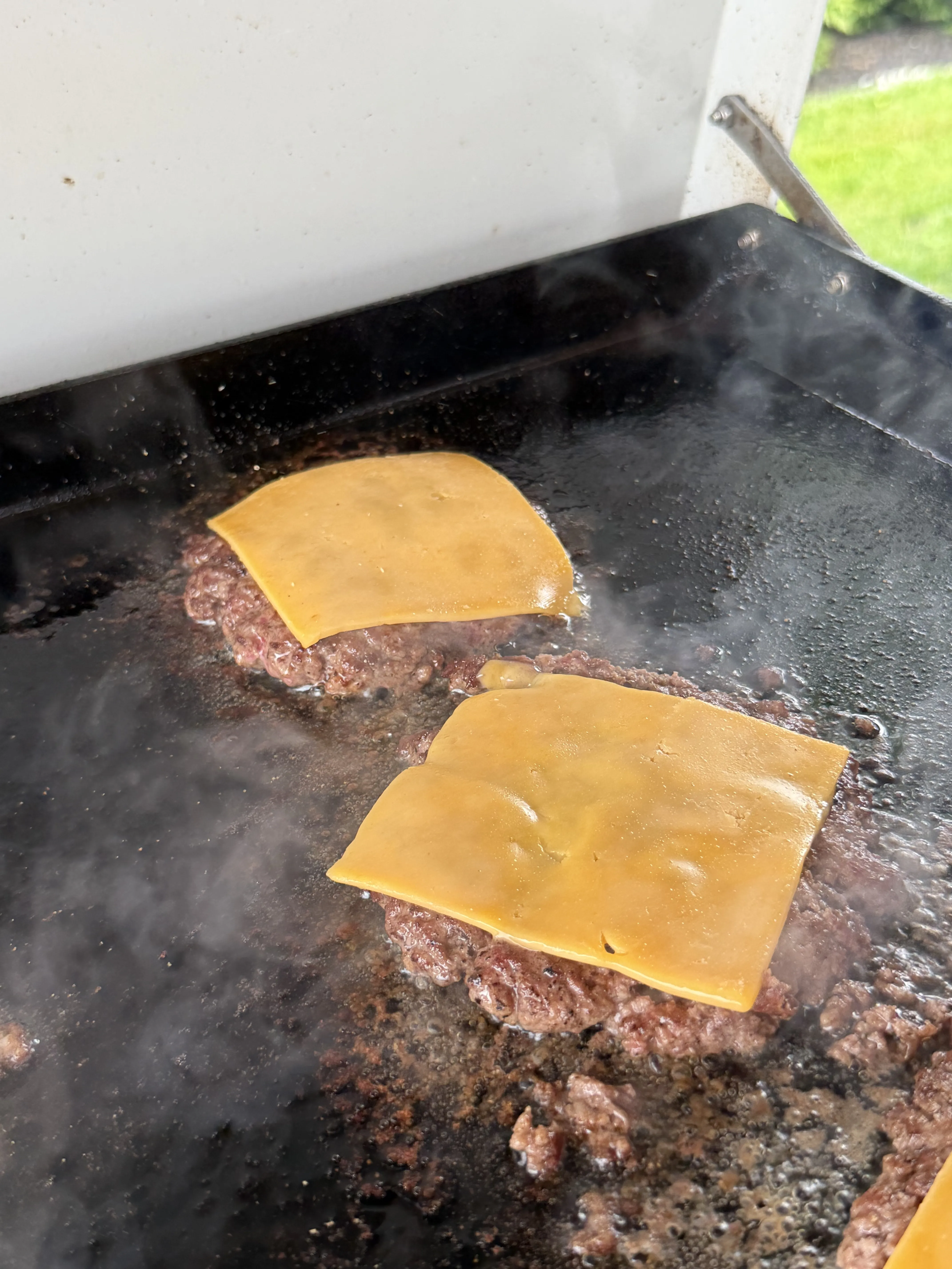 American cheese melting over smash burger patties on a hot flat top griddle