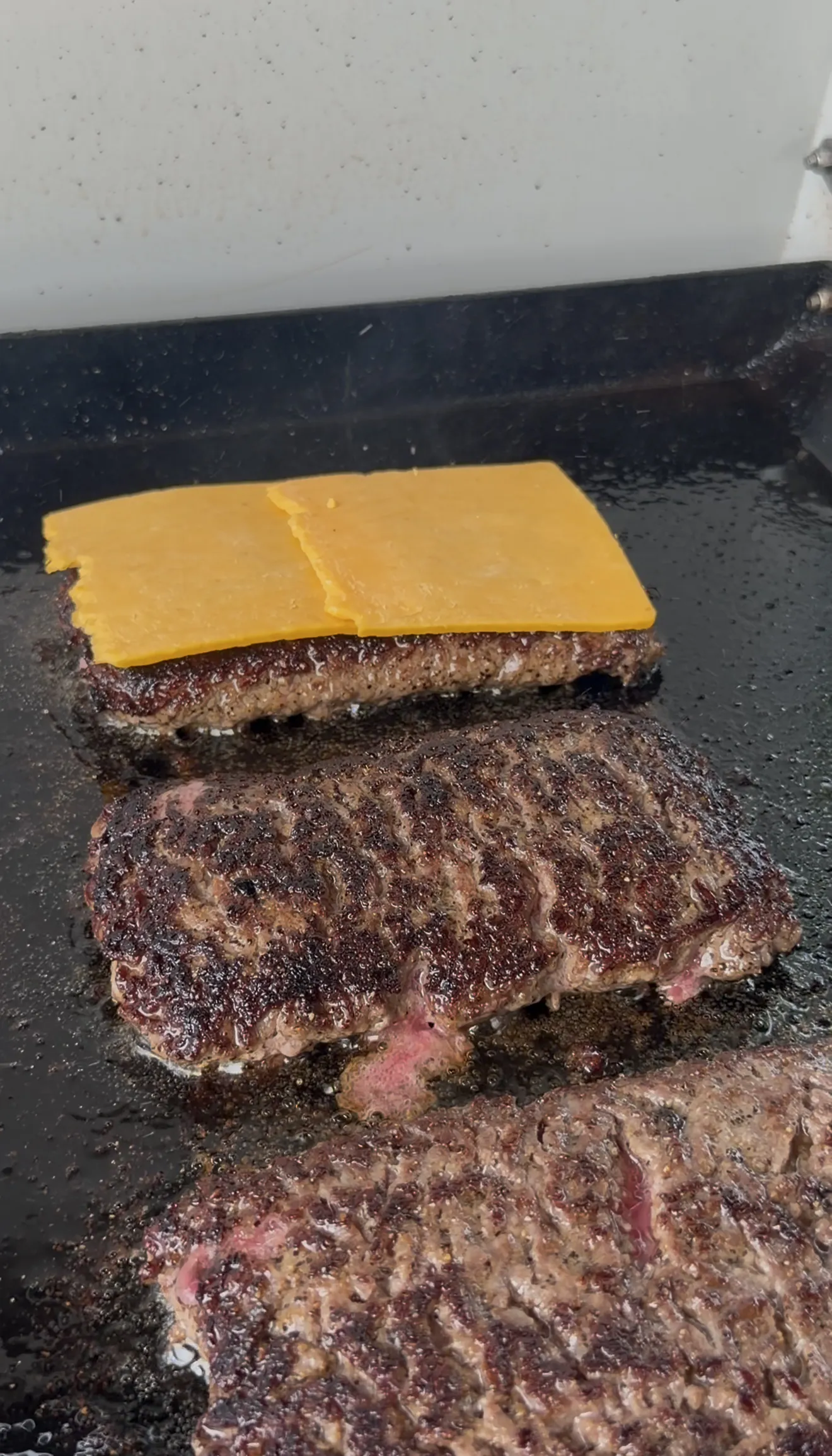 Bacon jam patty melts with melted cheese cooking on a black griddle