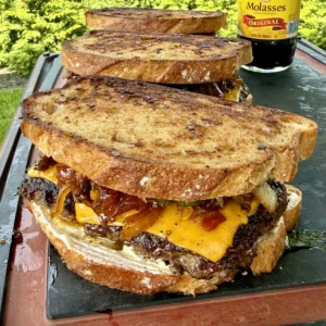 Stack of bacon jam patty melts with melted cheese on toasted bread, served on slate board with molasses bottle