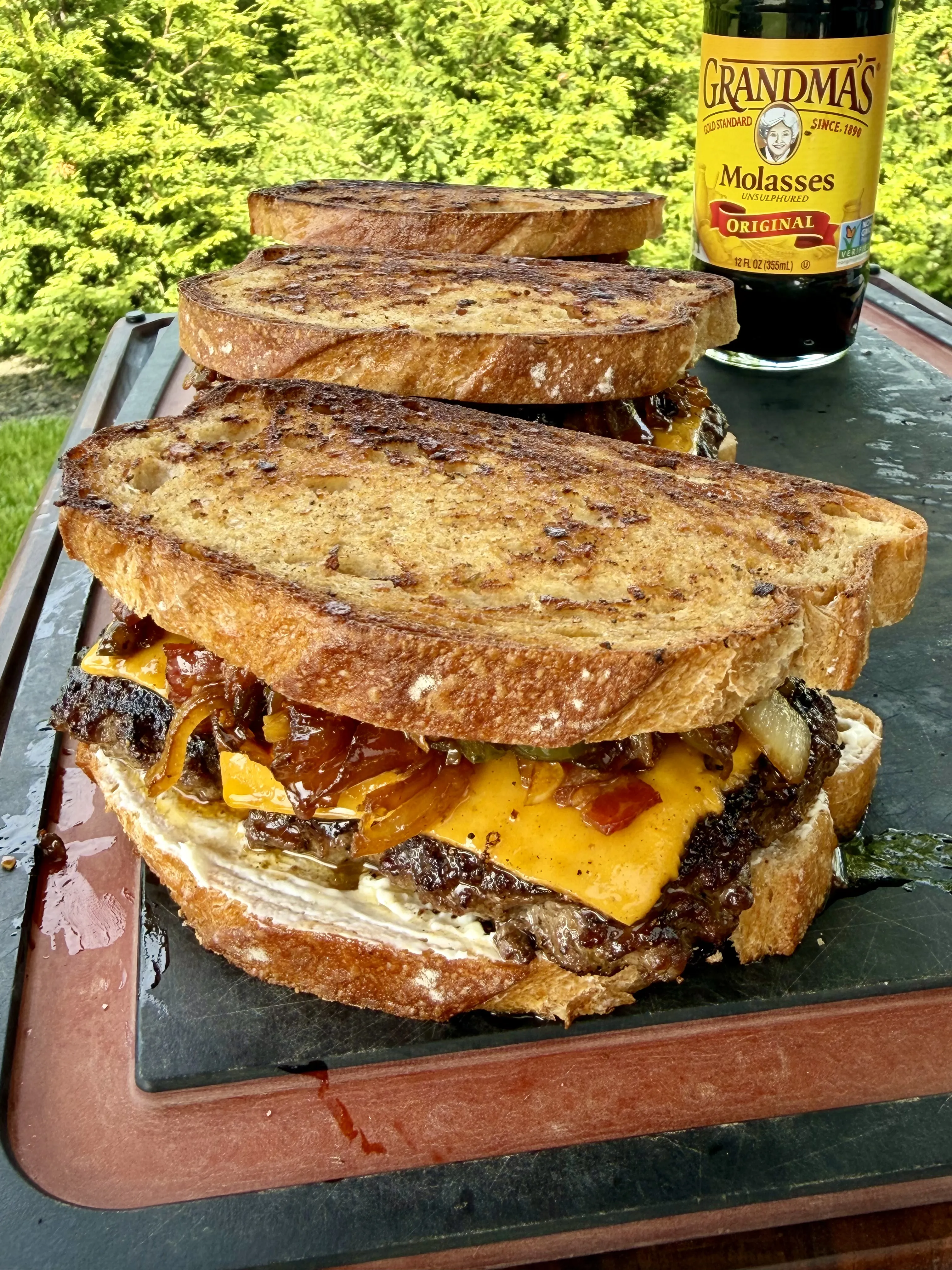 Stack of bacon jam patty melts with melted cheese on toasted bread on a slate board