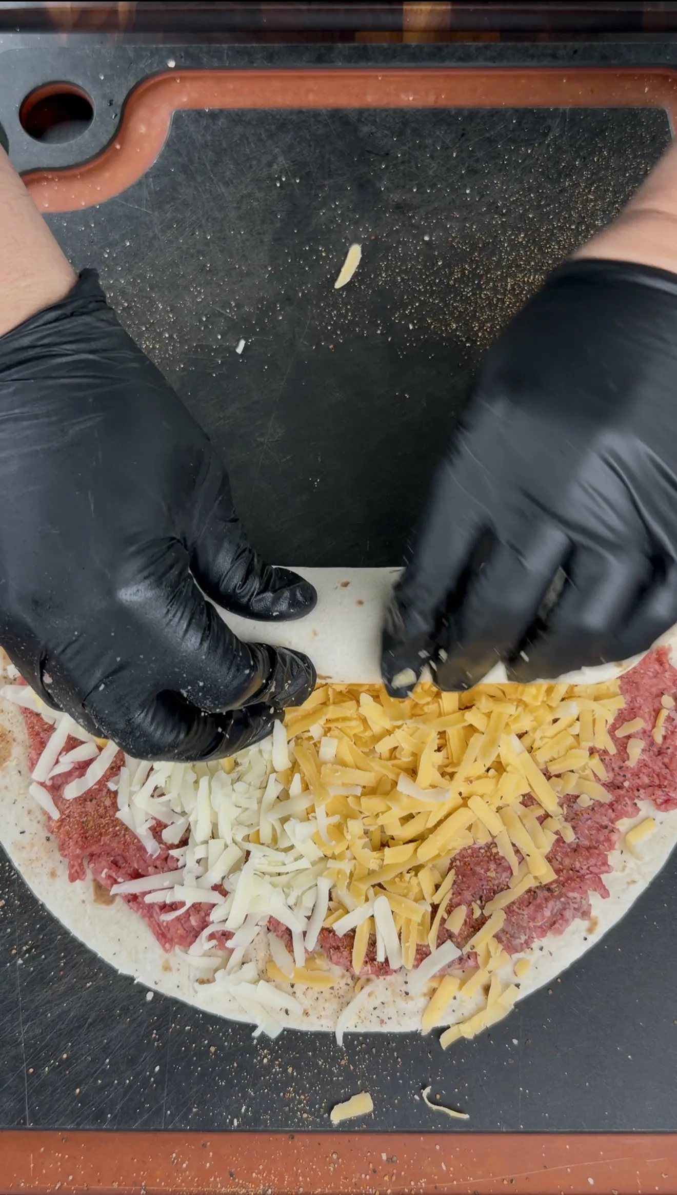 Shredded cheese being spread over seasoned ground beef on a flour tortilla for cowboy butter pinwheels
