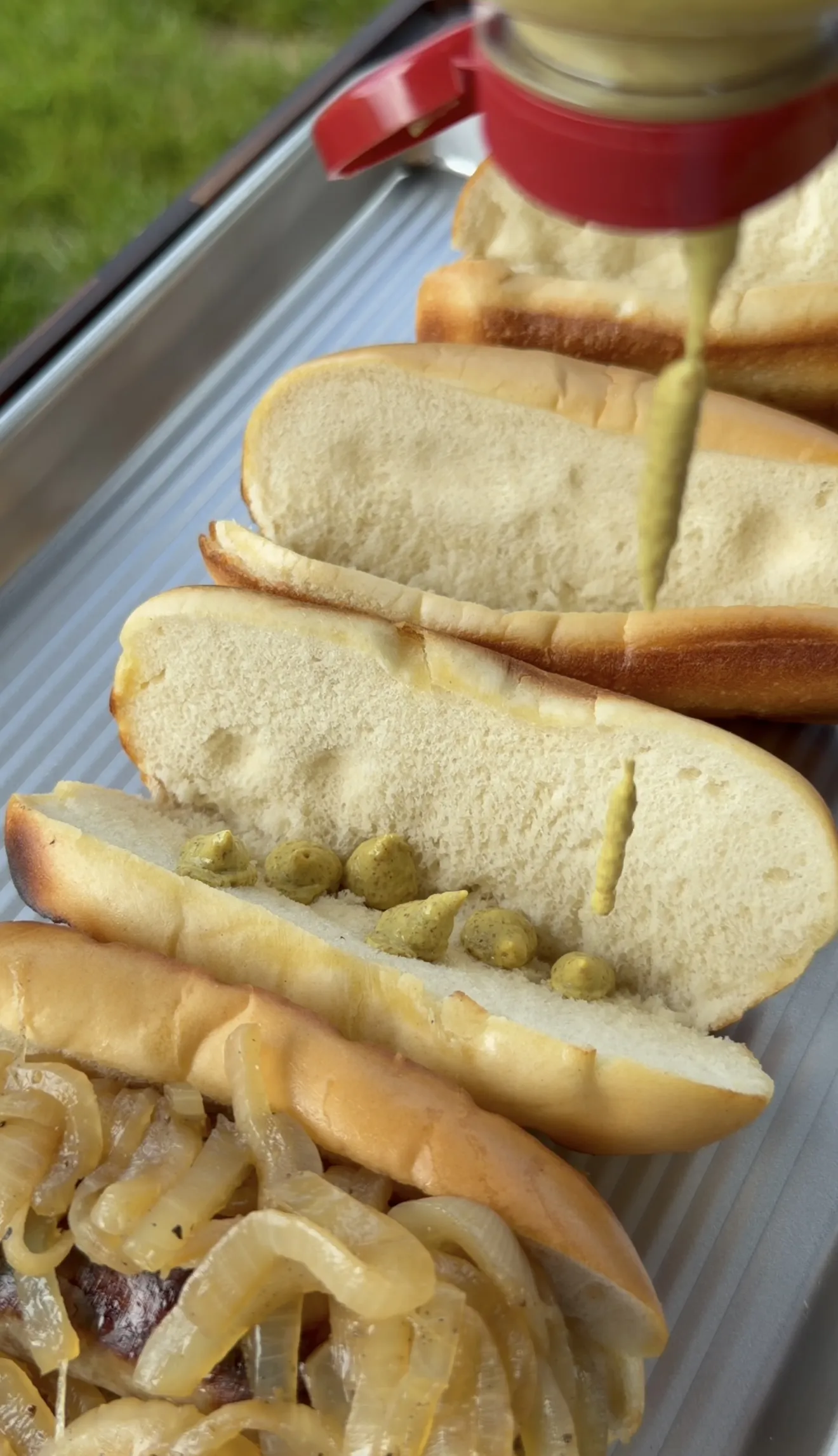 Spicy brown mustard being squeezed onto buns filled with beer brats and caramelized onions