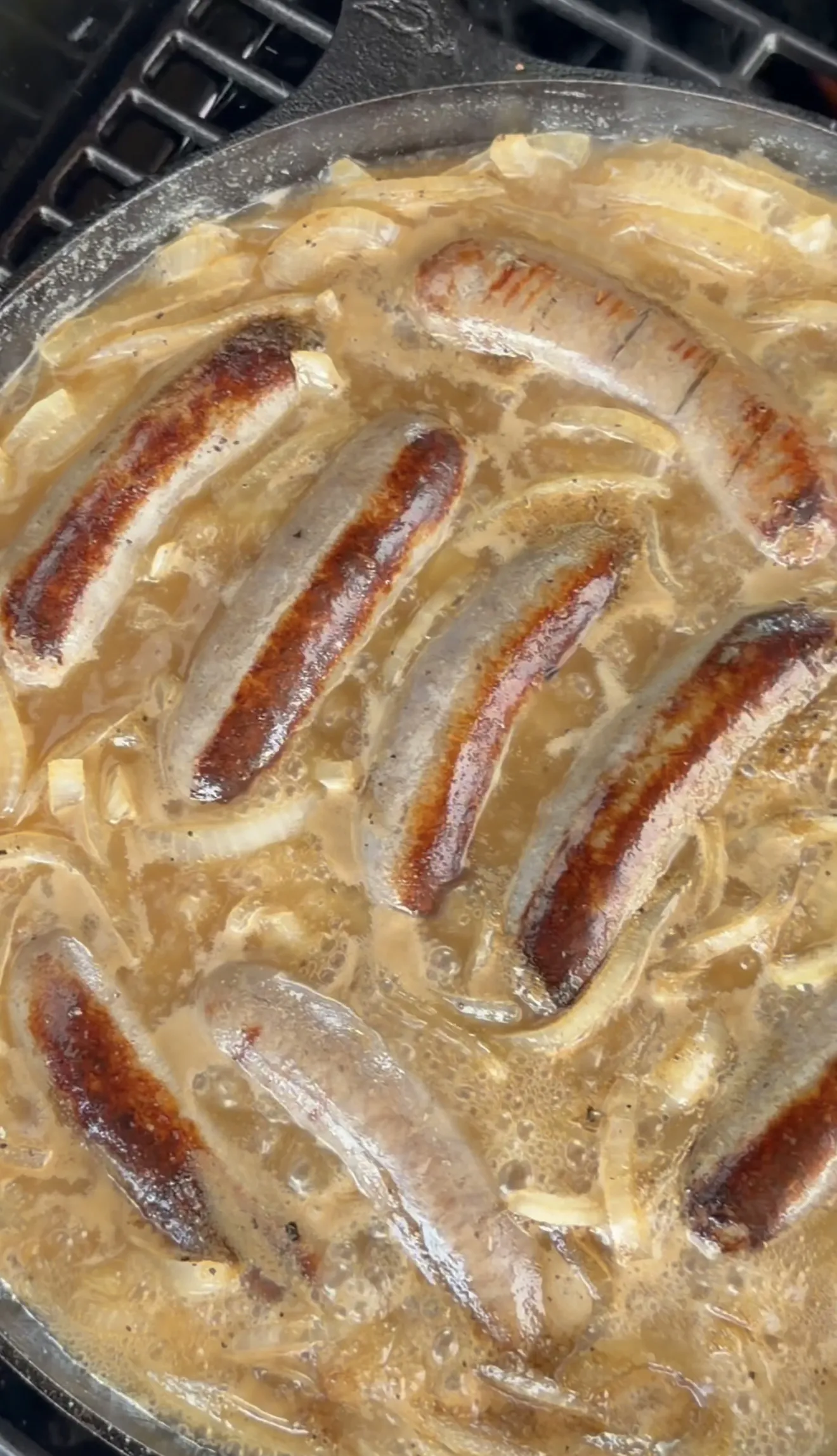 Beer brats simmering with caramelized onions in a bubbling beer sauce in a cast iron skillet