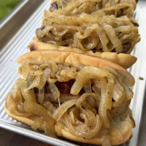 Beer-braised brats topped with golden caramelized onions served in toasted hoagie rolls on a silver baking tray