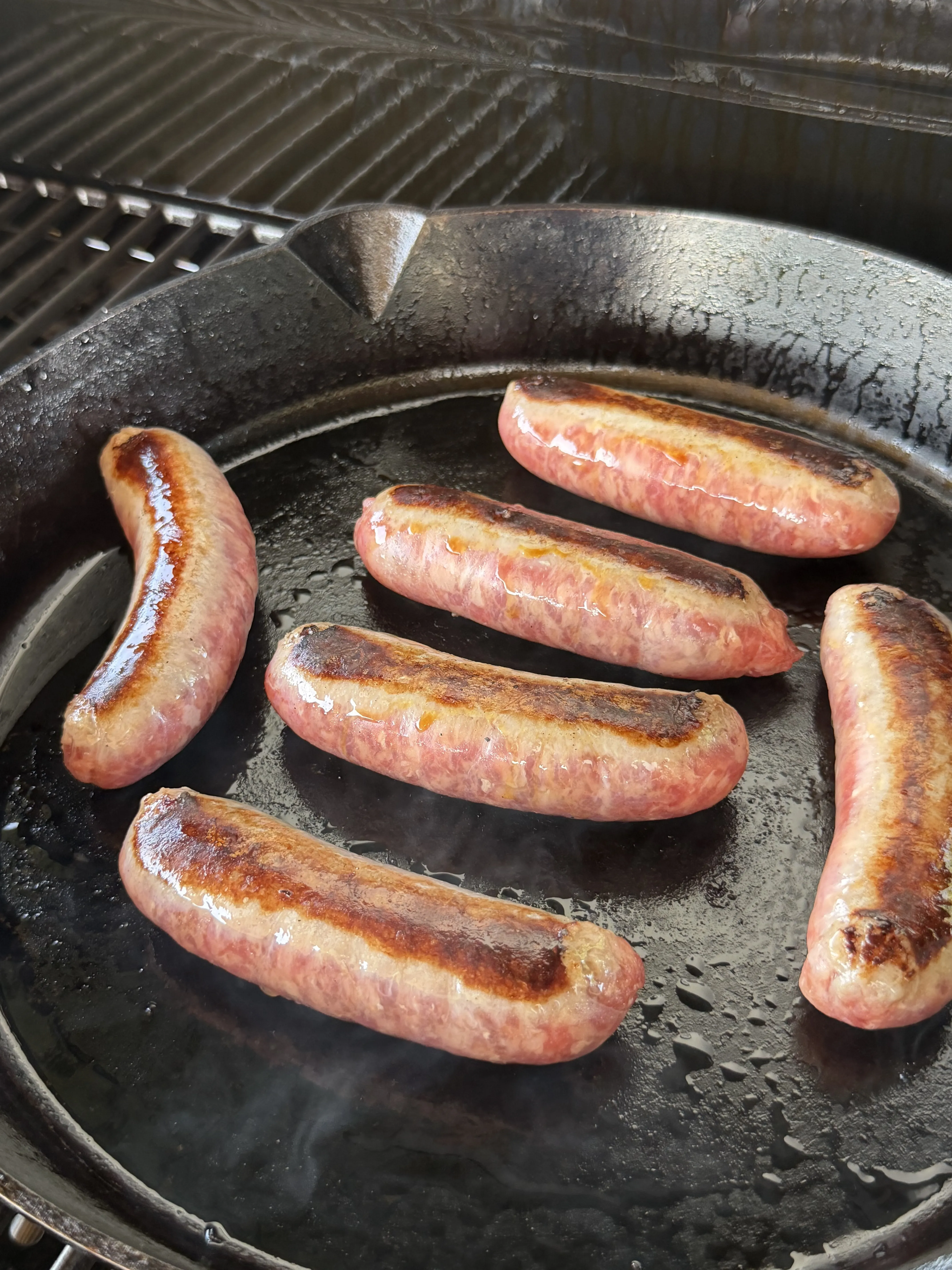 Six brats searing with golden-brown caramelized grill marks in a cast iron skillet