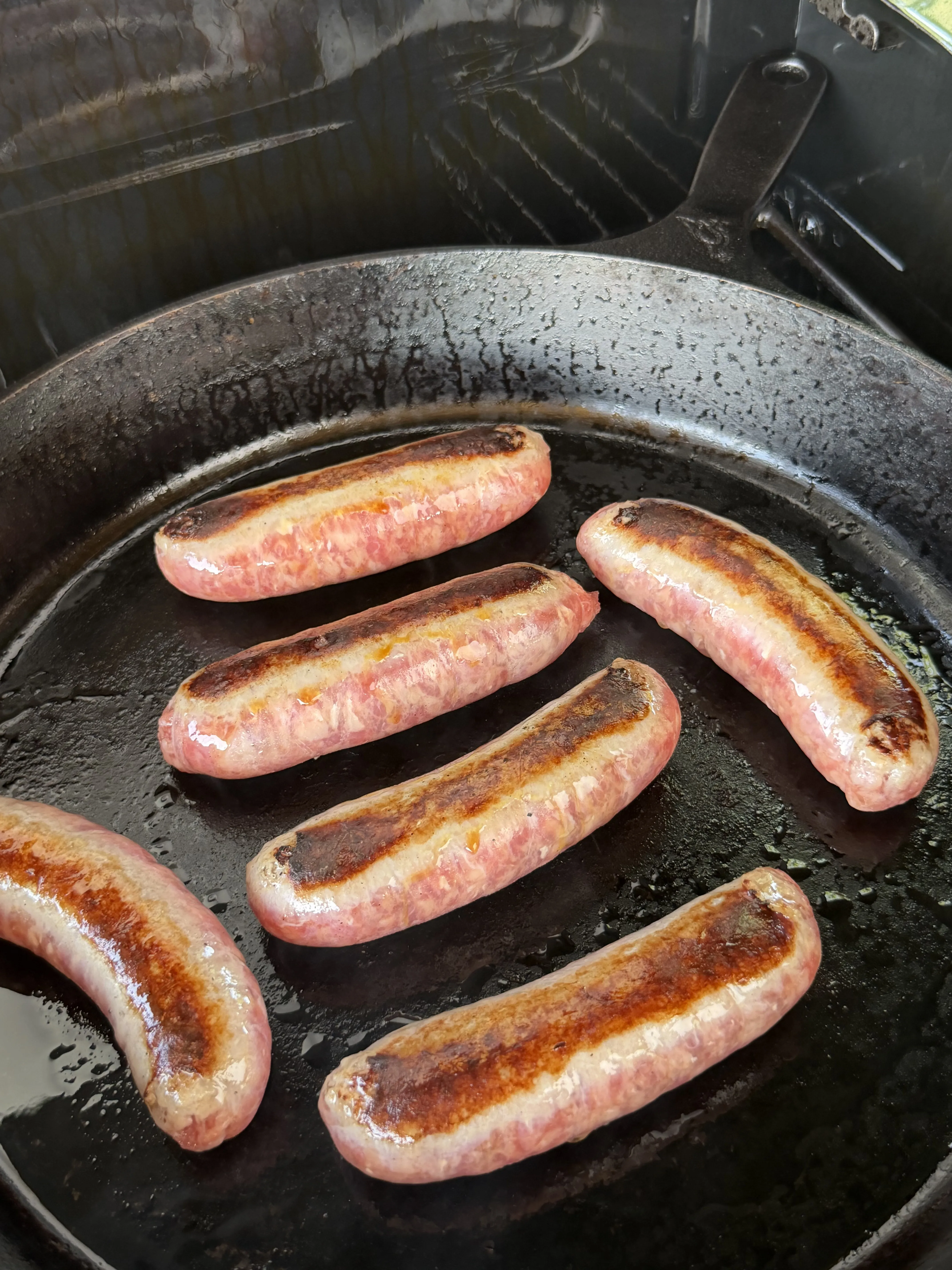 Six bratwurst sausages searing with golden-brown caramelized edges in a cast iron skillet