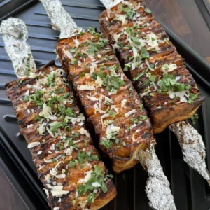 Grilled buffalo chicken tortilla kebabs topped with shredded cheese and fresh herbs on a black grill pan