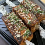 Grilled buffalo chicken tortilla kebabs topped with shredded cheese and fresh cilantro on a black grill tray