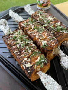 Grilled buffalo chicken tortilla kebabs topped with shredded cheese and fresh cilantro on a black grill tray