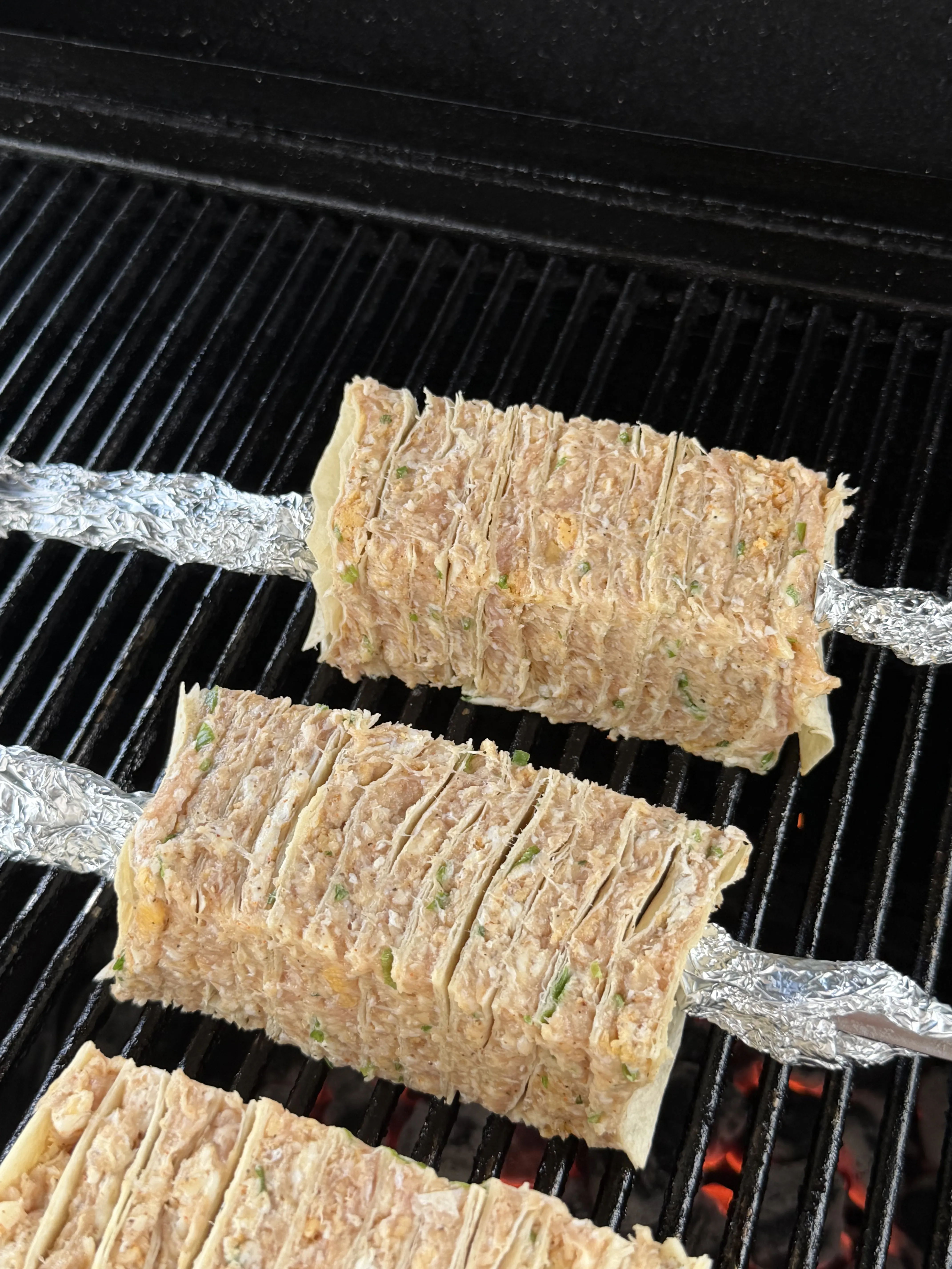 Buffalo chicken tortilla kebabs lined up and cooking on the grill