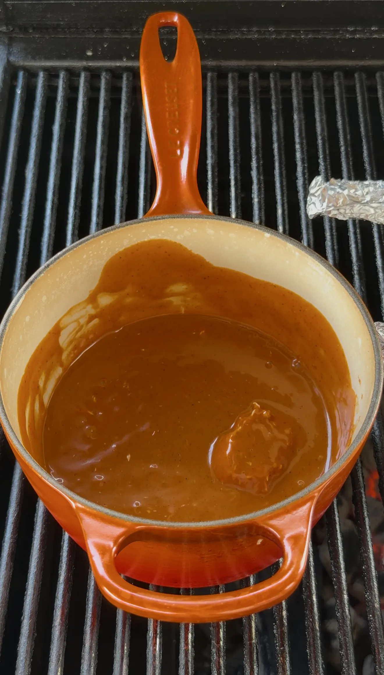 Buffalo sauce and butter warming together in an orange pot on the grill