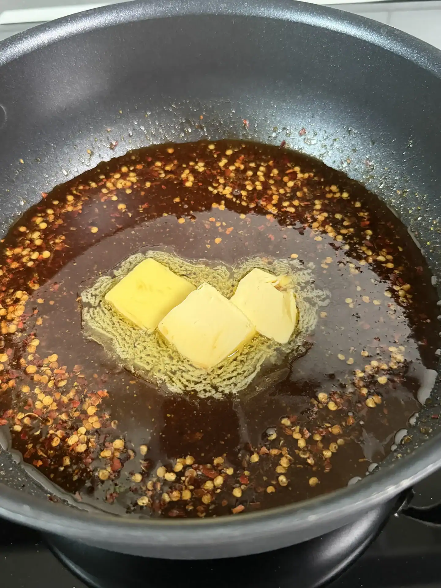 Butter melting in a dark pan with red pepper flakes and honey.