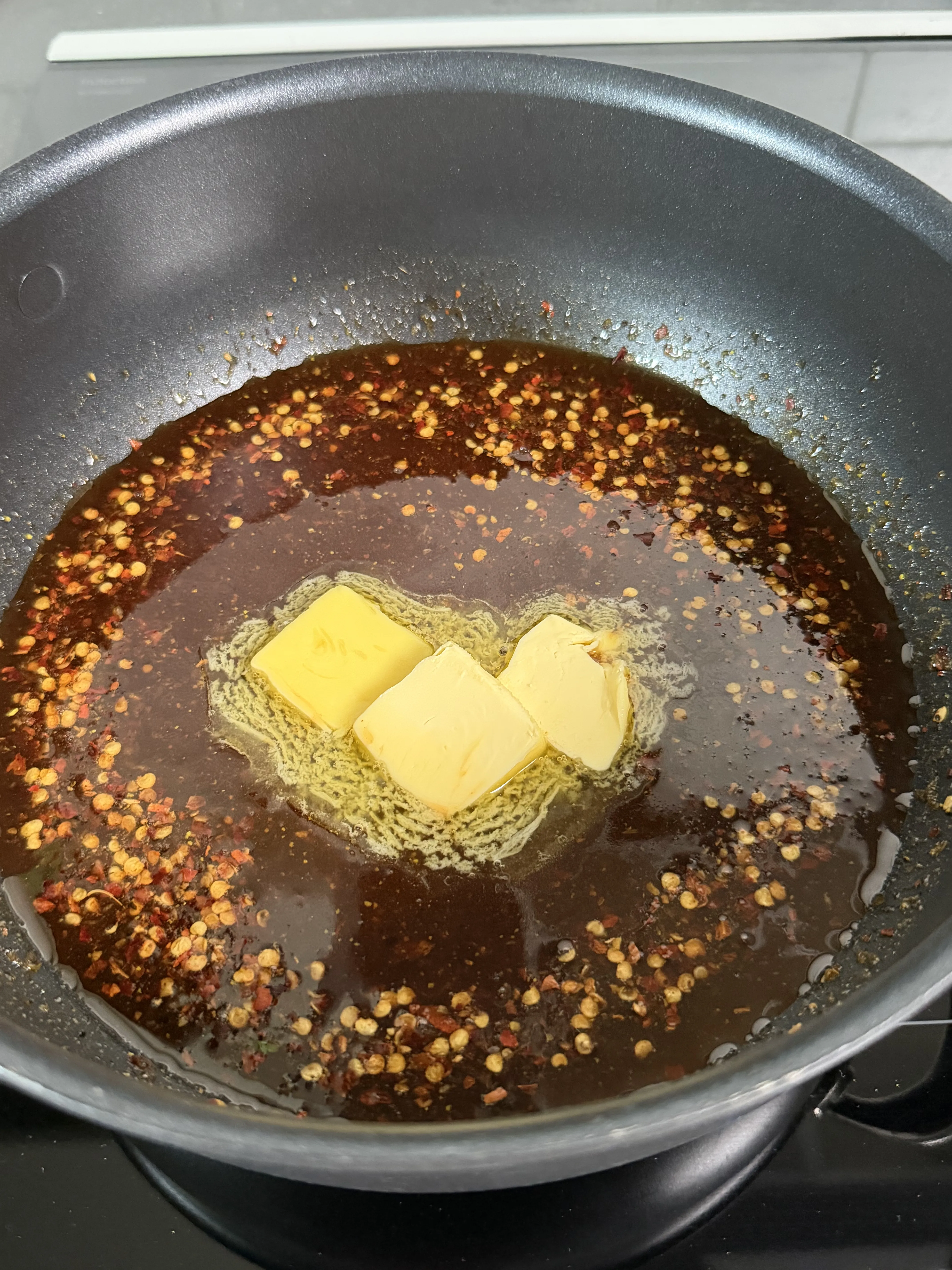 Butter melting into the hot honey lemon pepper glaze with visible spices in a saucepan