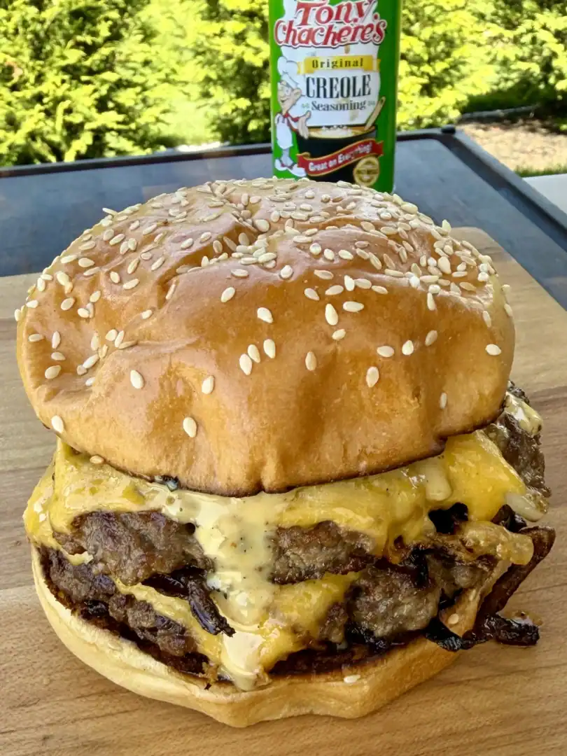 Cajun Oklahoma onion smash burger with melted cheese on sesame bun, Tony Chachere's Creole seasoning in background