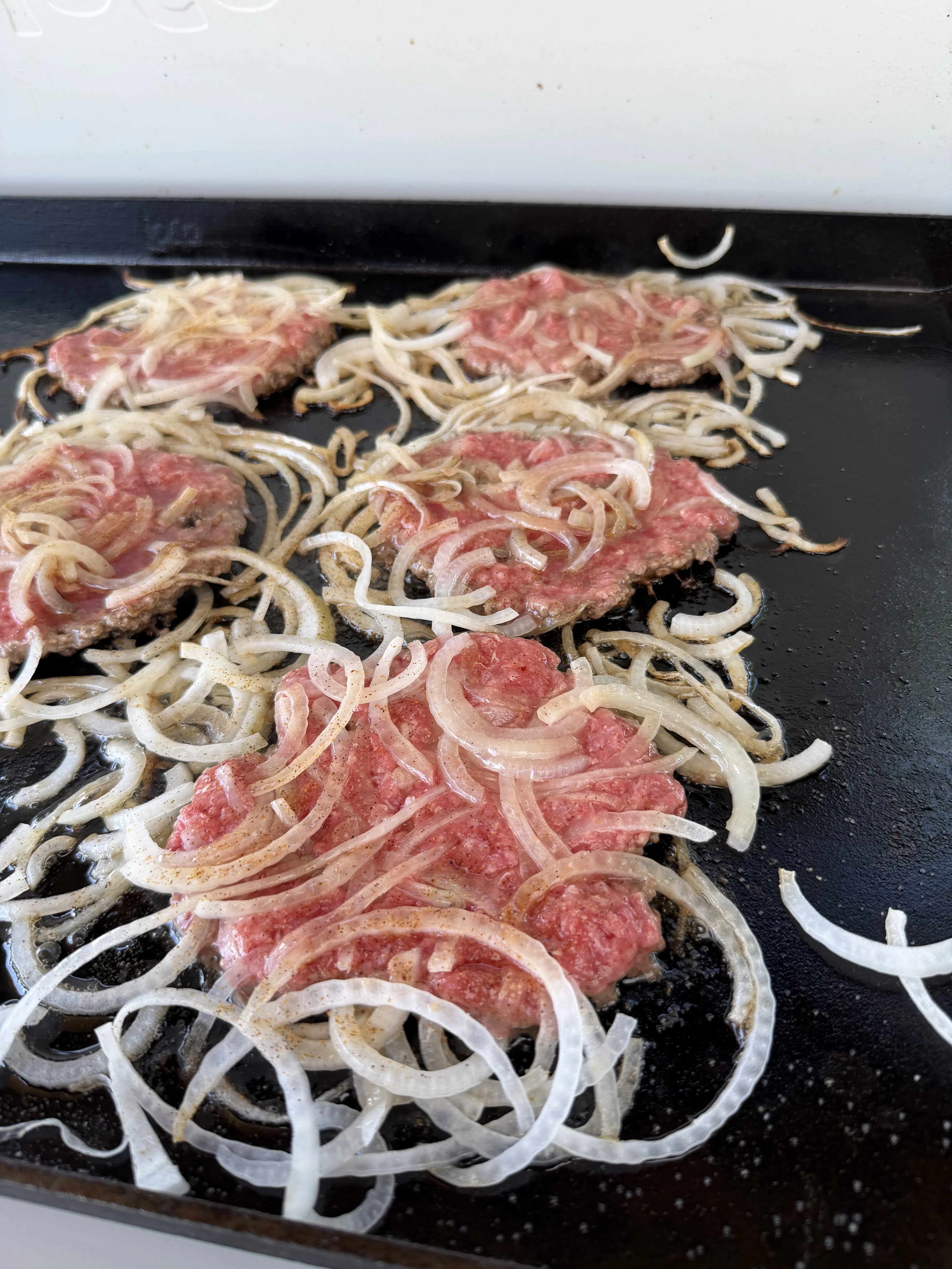Cajun smash burgers smashed thin with shaved onions pressed into the beef on the griddle