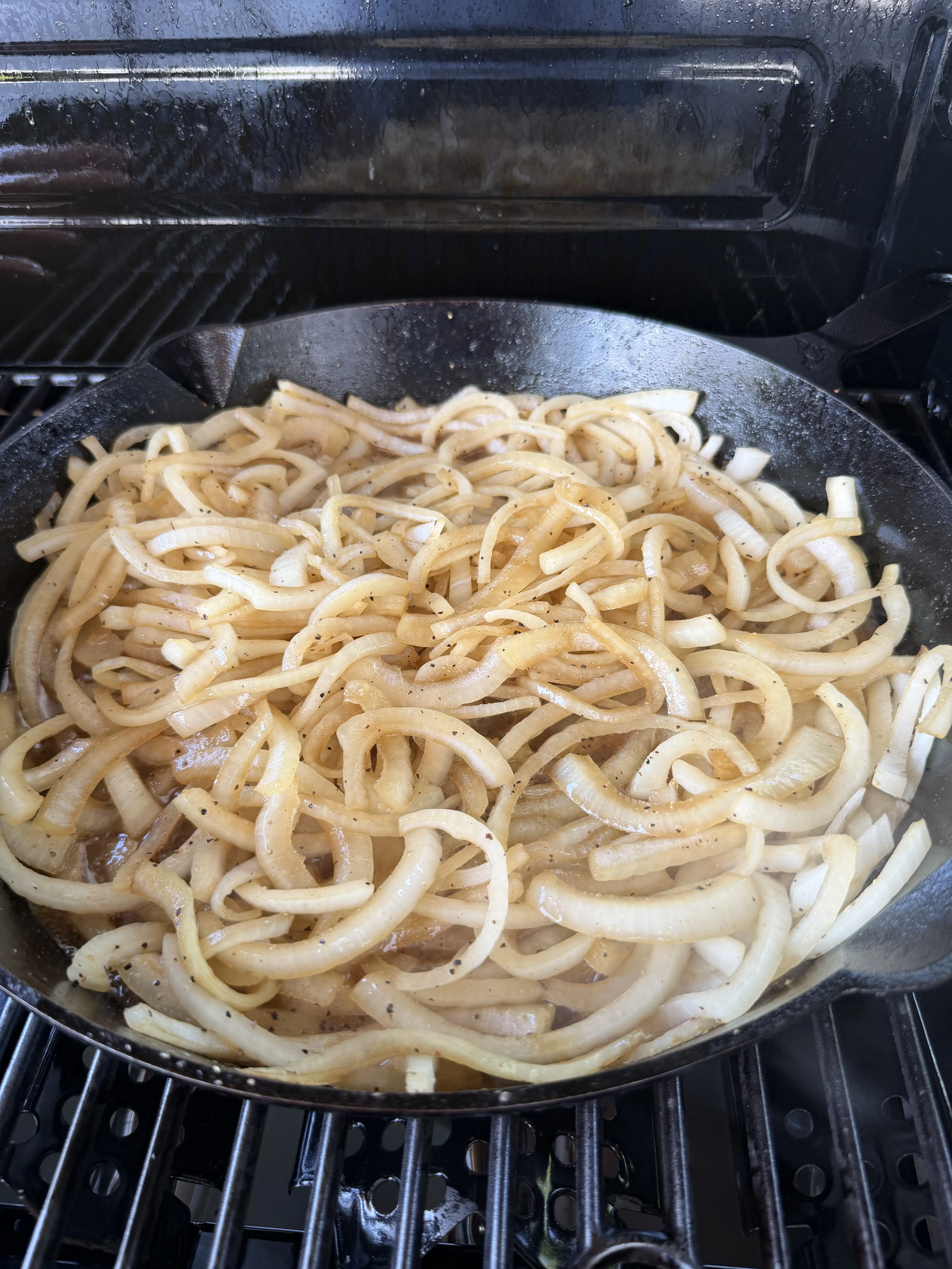 Sliced onions caramelizing in a cast iron skillet on a gas grill seasoned with black pepper