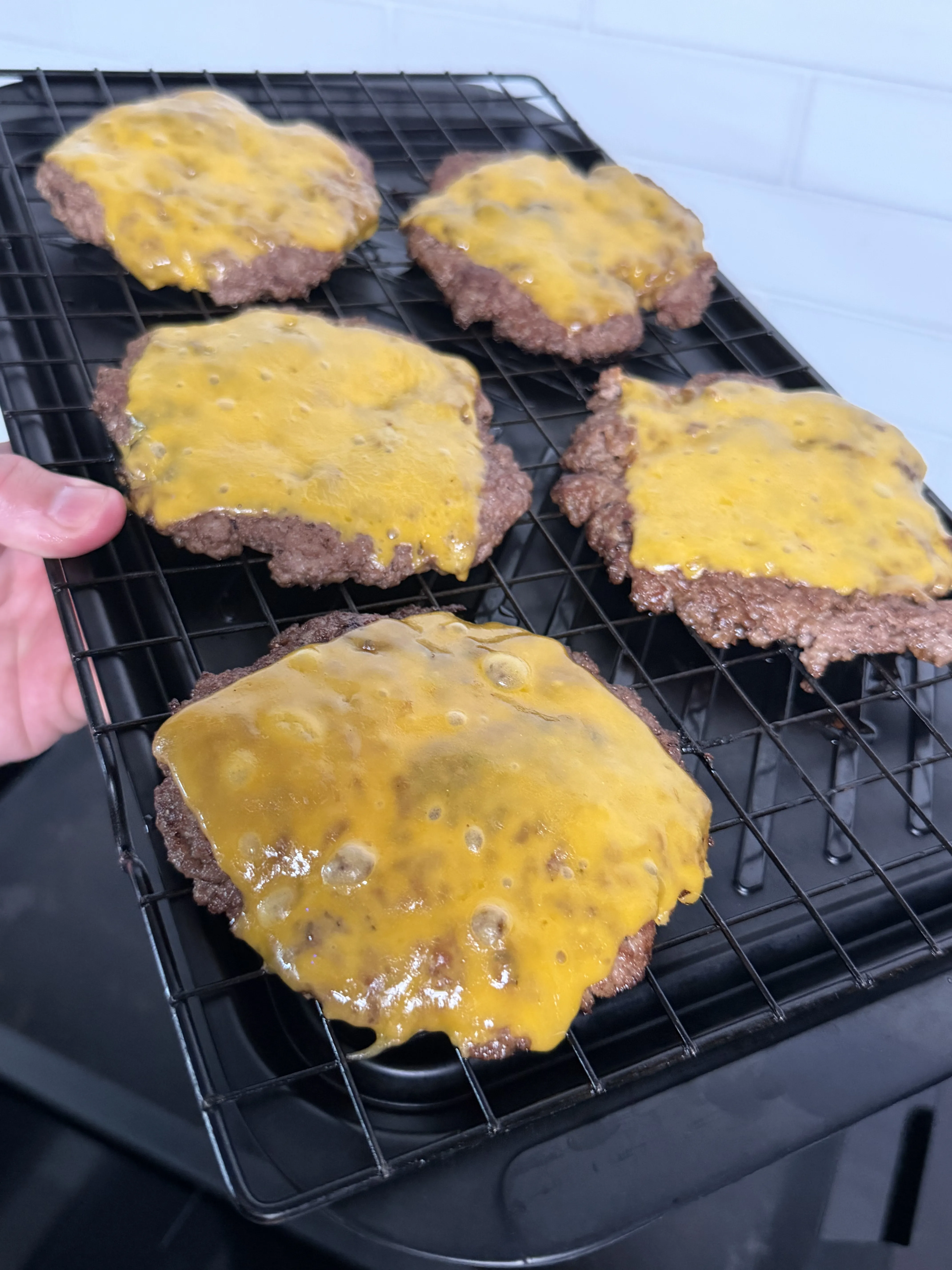Smashed beef burger patties topped with melted cheese on a cooling rack
