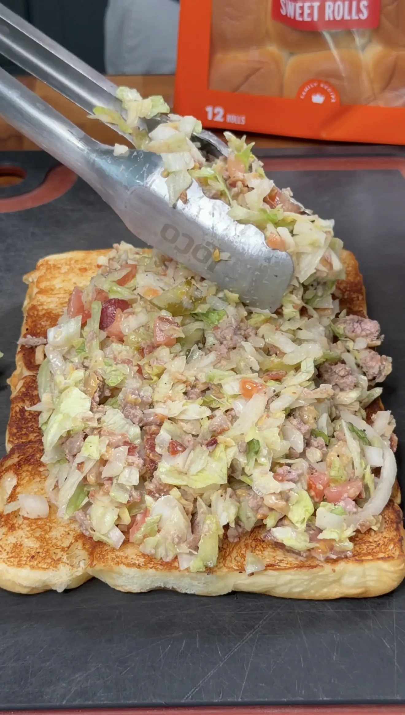 Chopped cheeseburger mixture of beef, lettuce, and tomato being loaded onto toasted slider rolls