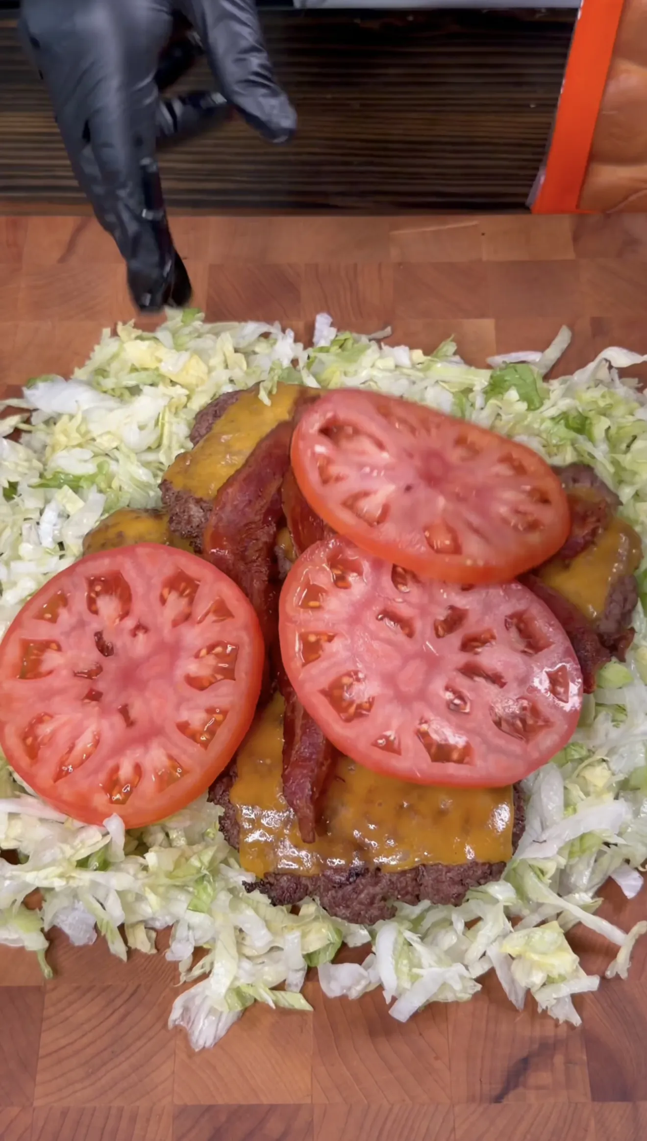 Smash burger patties with melted cheese, fresh tomato, and shredded lettuce ready to chop