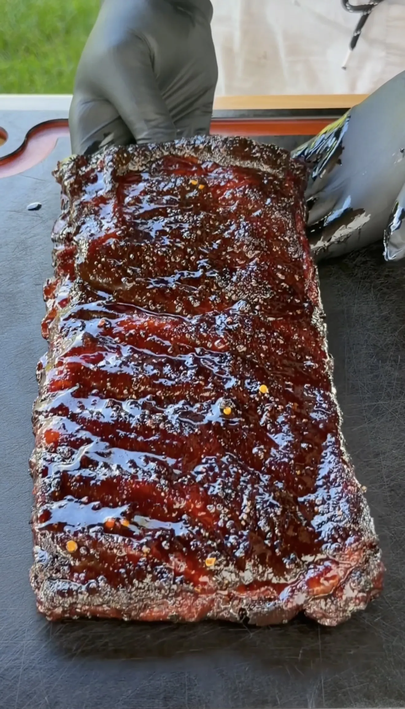 A full rack of competition style smoked spare ribs coated in glossy BBQ sauce on a cutting board