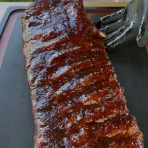 Full rack of competition-style smoked spare ribs with glossy BBQ glaze on a black cutting board