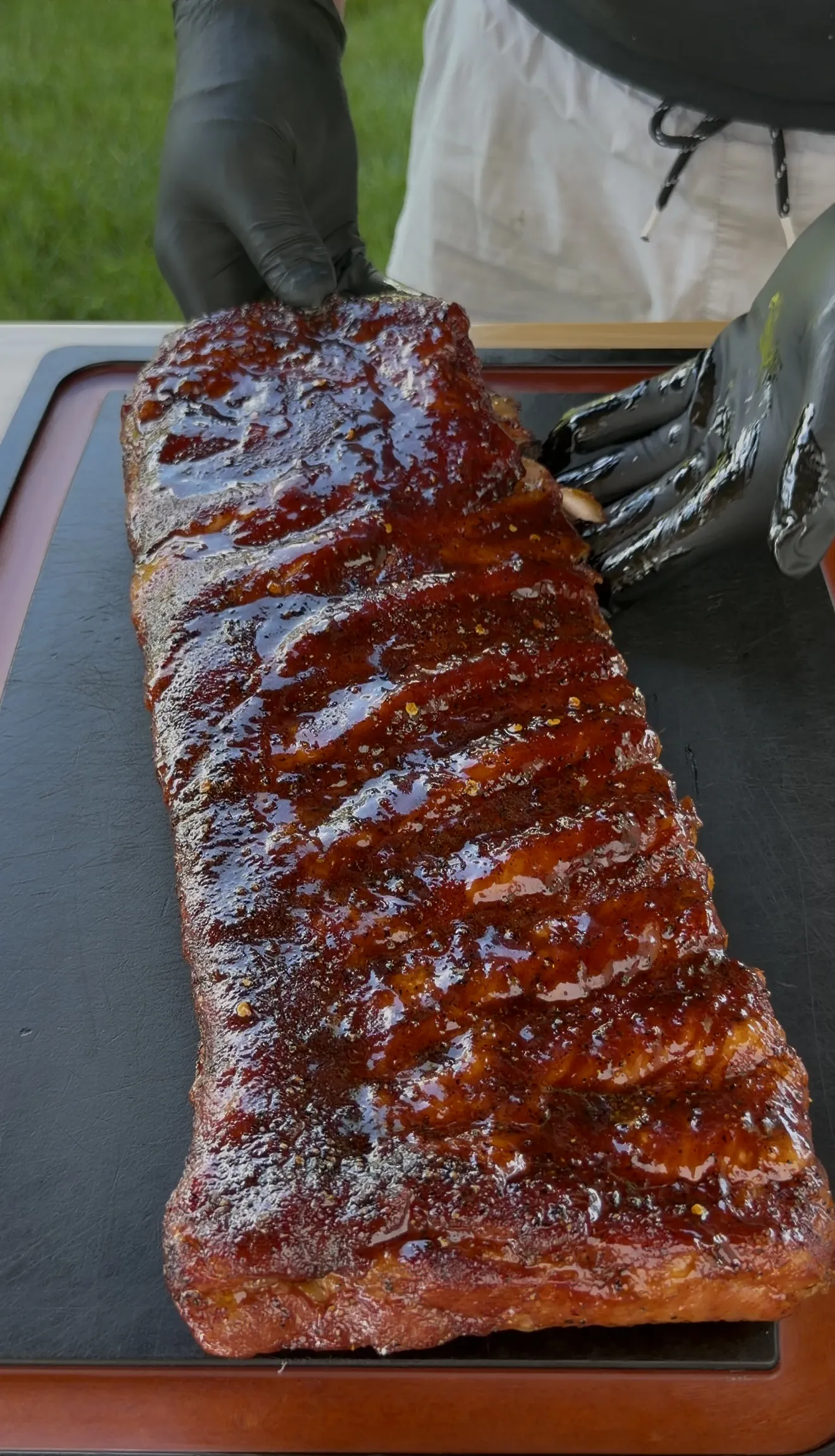 Full rack of competition style smoked spare ribs with glossy glaze on a cutting board