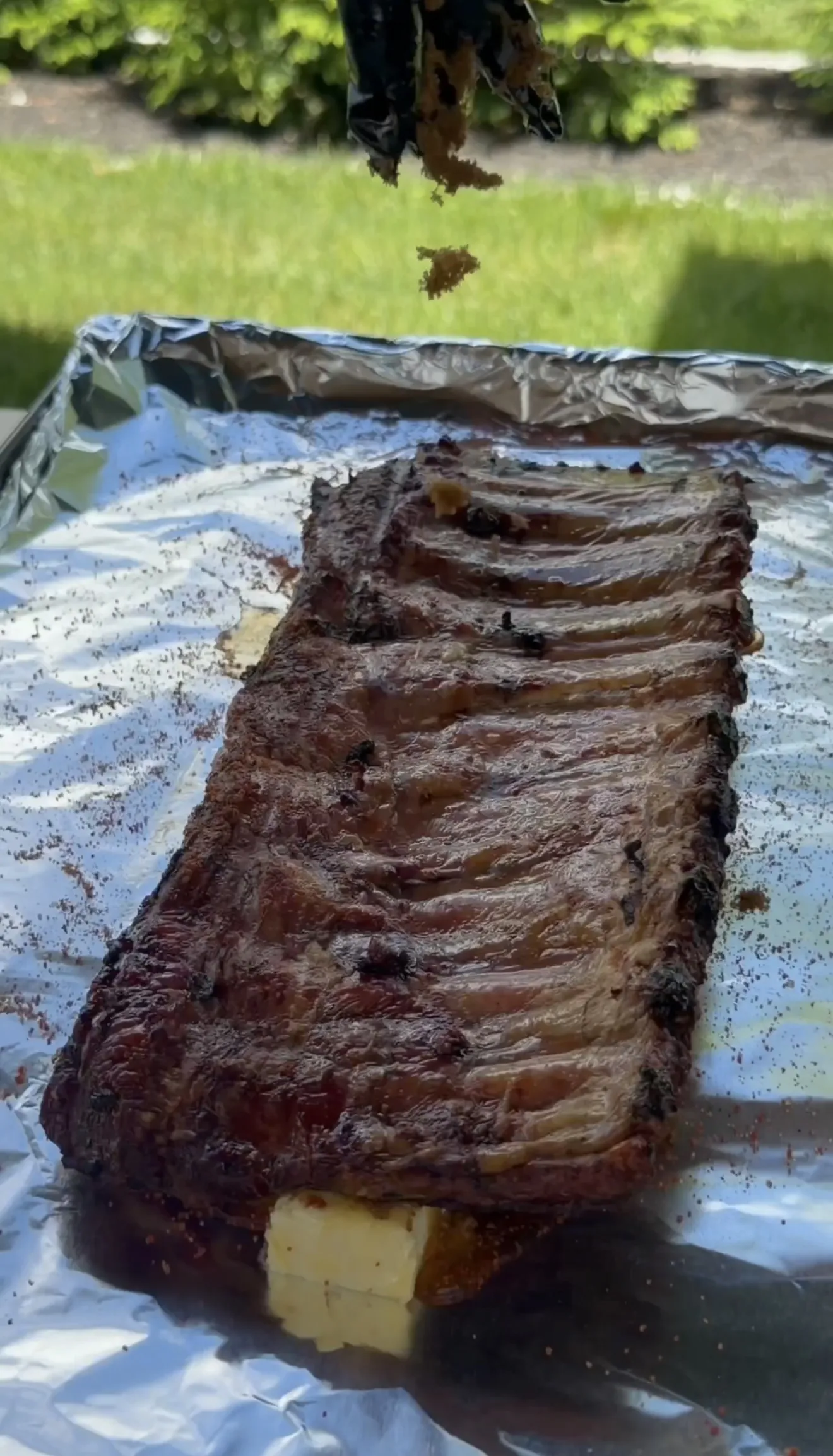 A rack of competition style smoked spare ribs resting on foil with butter melting underneath