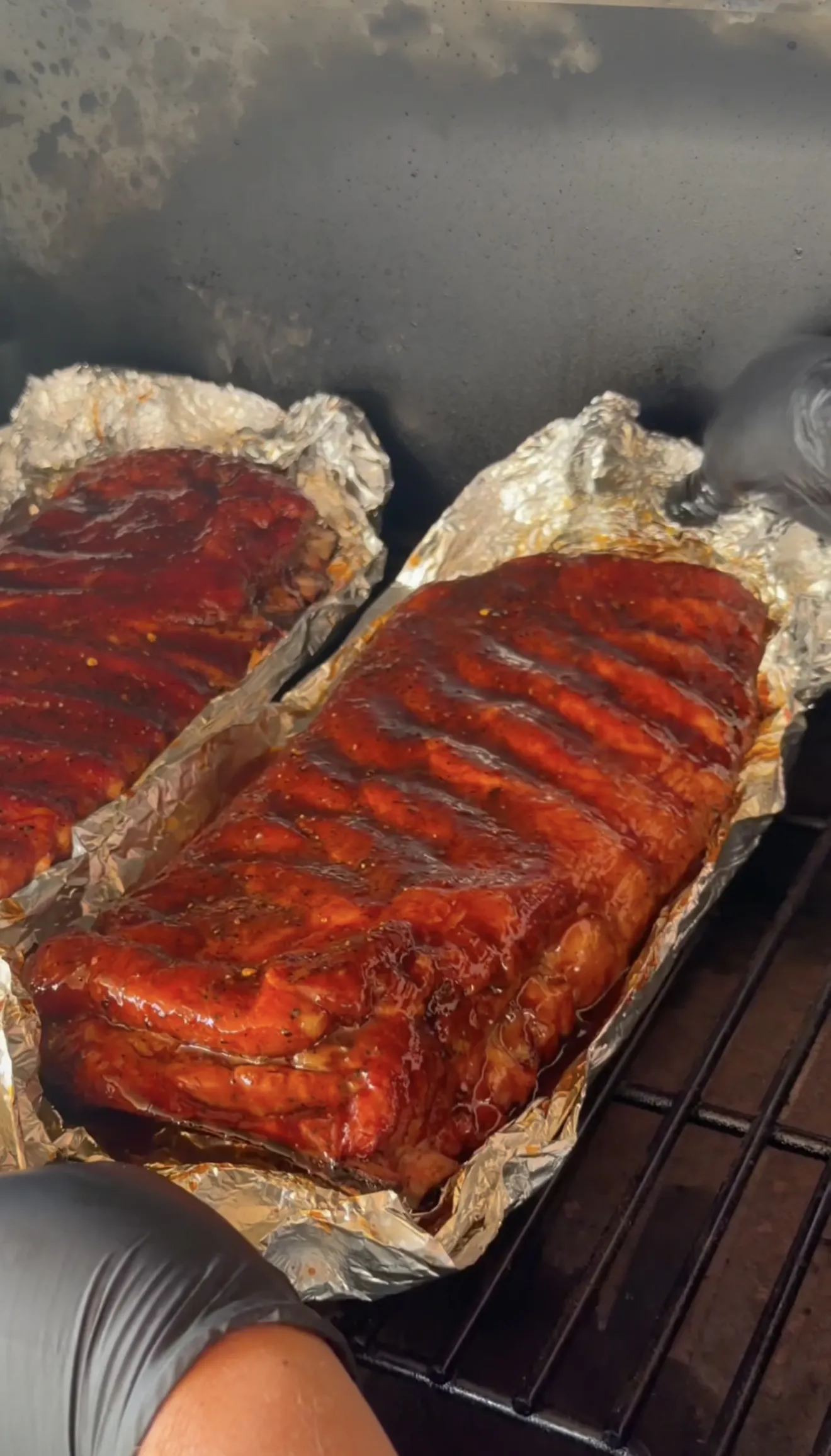 Glazed competition style smoked spare ribs with caramelized BBQ sauce setting on a smoker grate