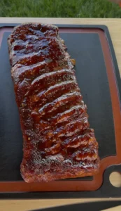 A full rack of competition-style smoked spare ribs with glossy BBQ glaze resting on a black cutting board