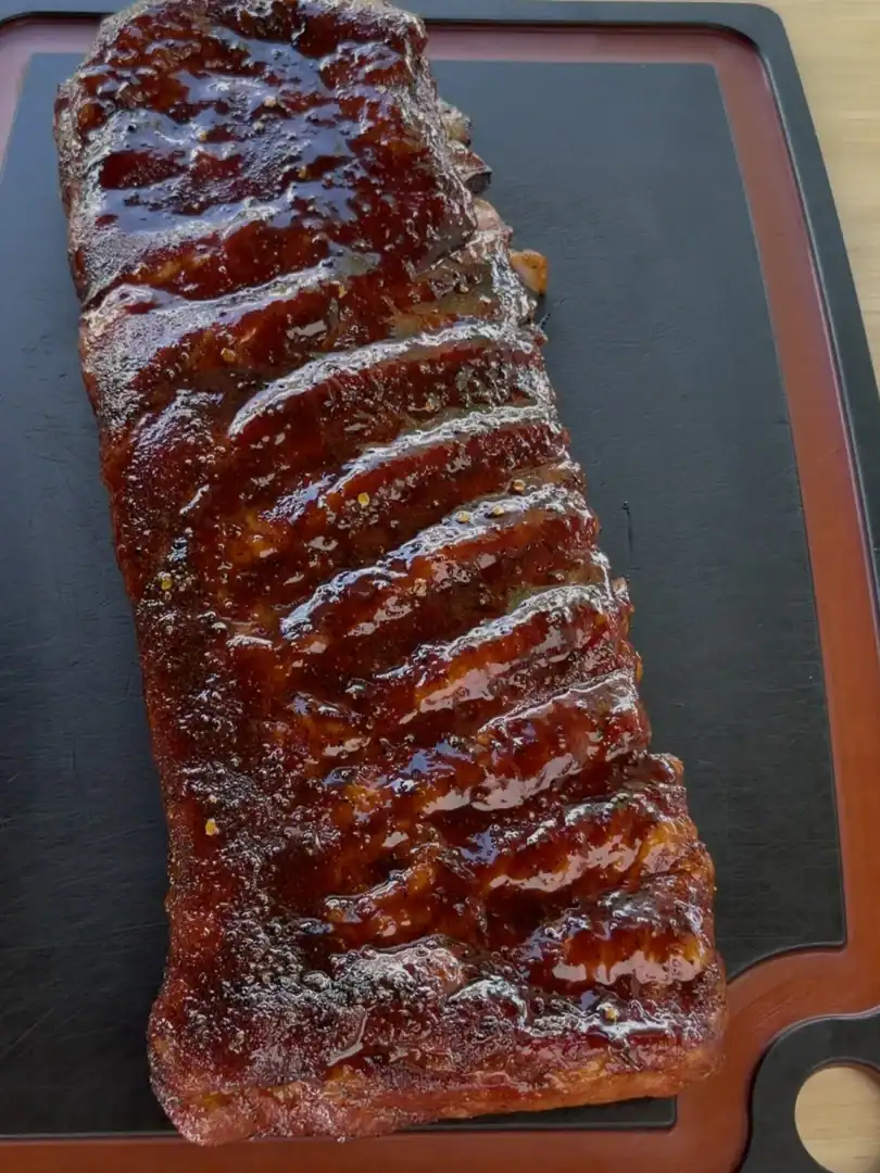 A full rack of competition-style smoked spare ribs with glossy BBQ glaze resting on a black cutting board
