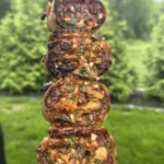 Grilled cowboy butter beef tortilla pinwheels stacked on a metal skewer, glazed with herb butter sauce