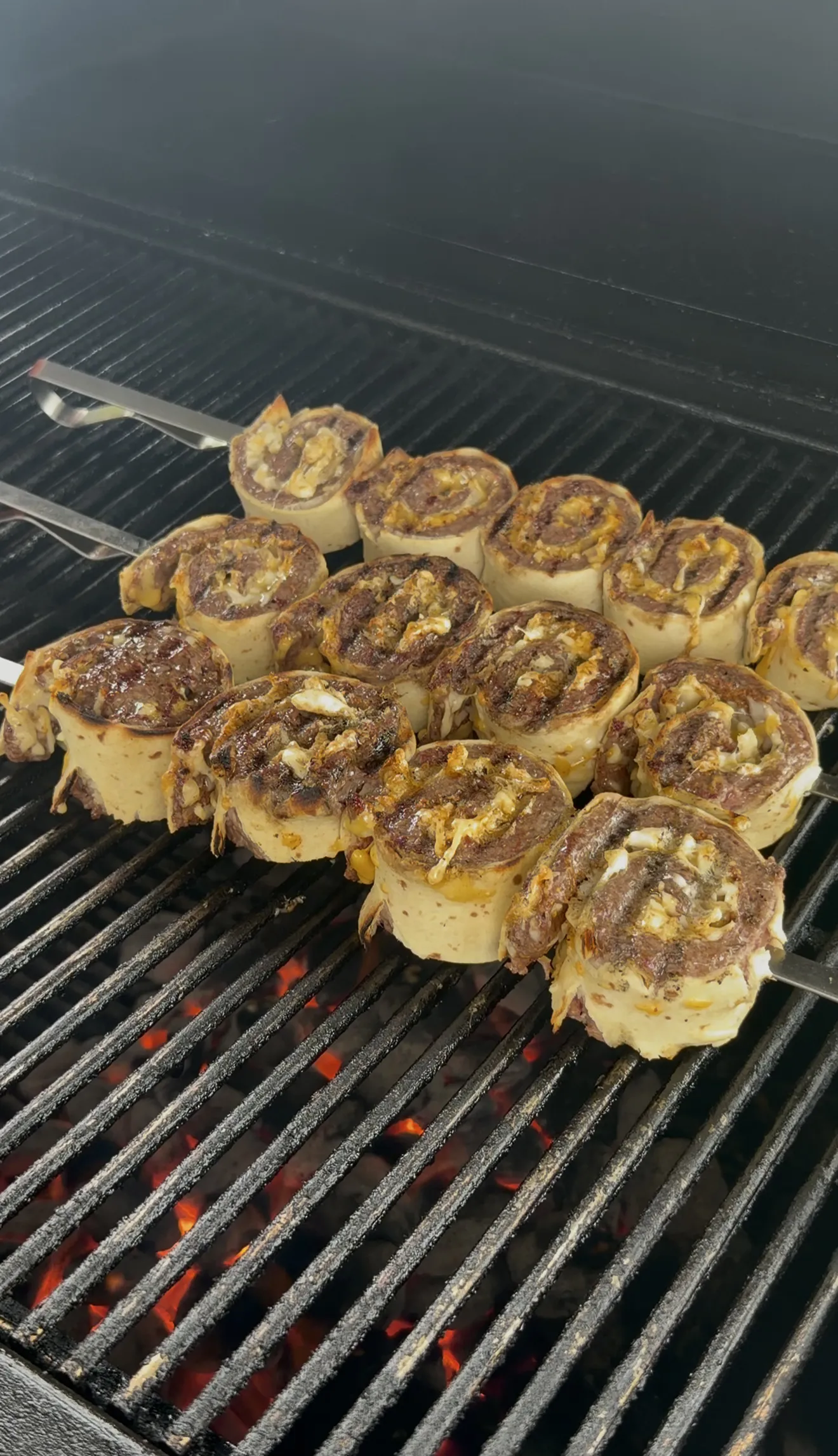 Cowboy butter beef tortilla pinwheels on metal skewers cooking over the grill
