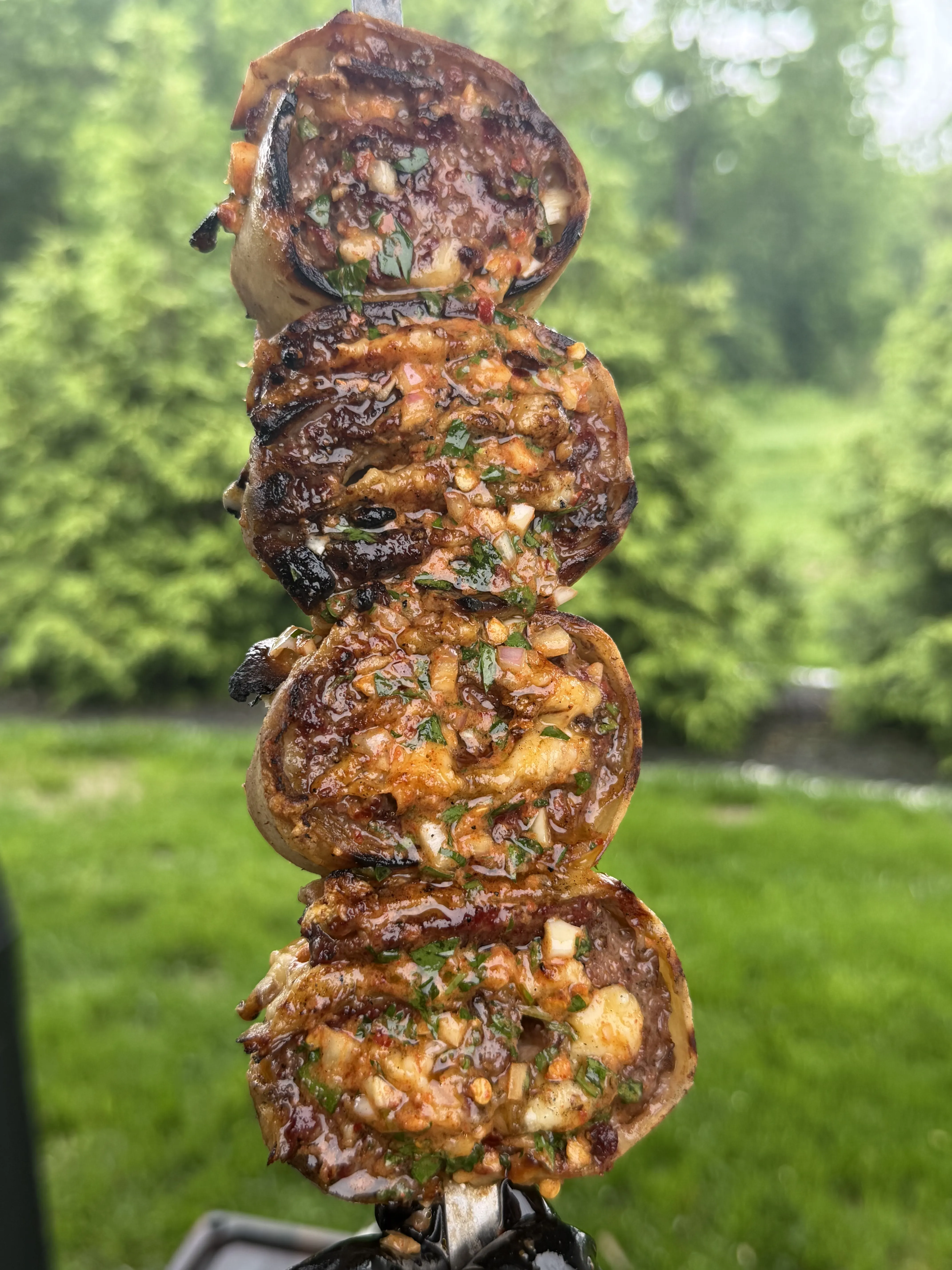 Grilled cowboy butter beef tortilla pinwheels stacked on a metal skewer with herb butter glaze