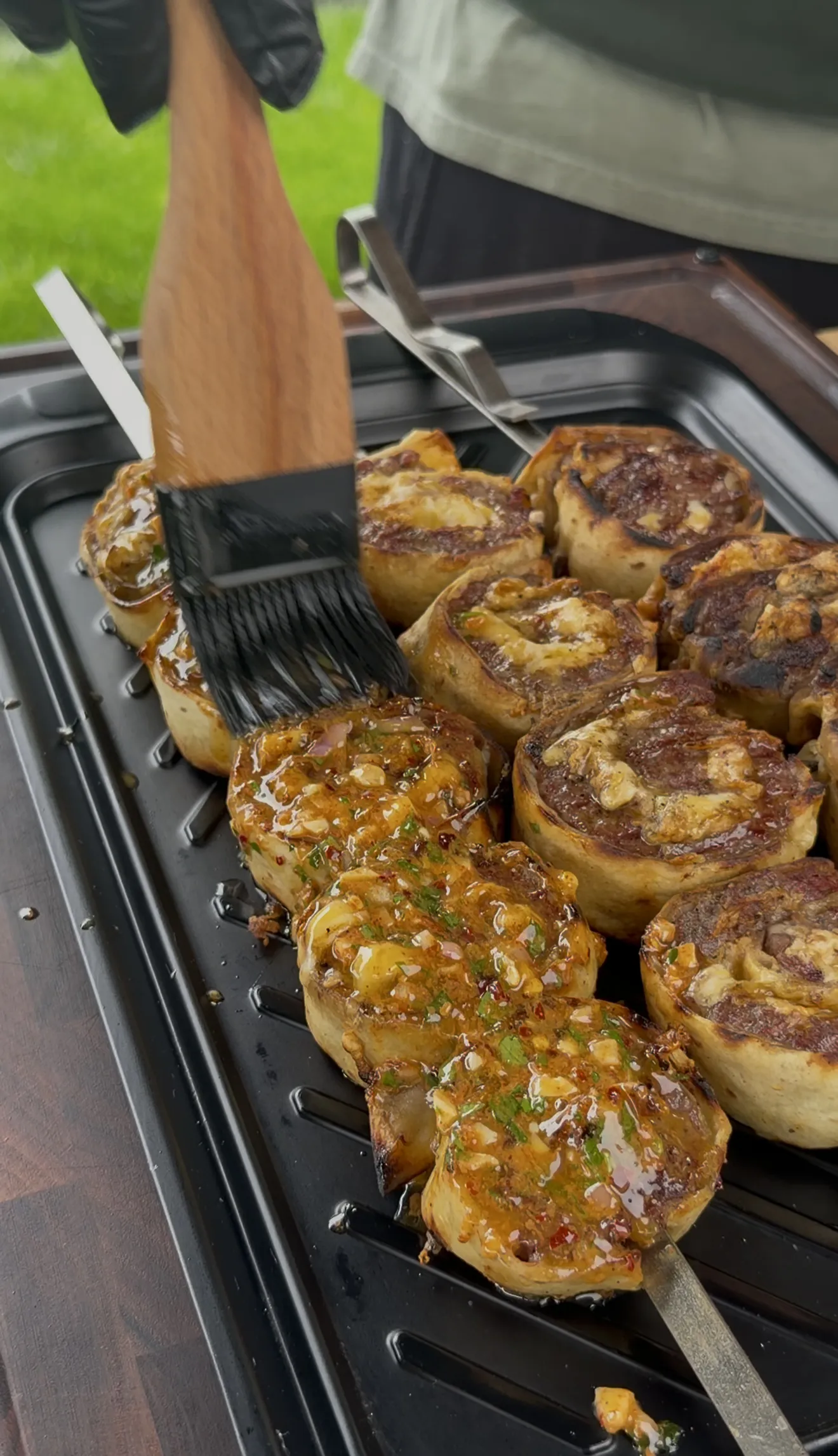 Beef tortilla pinwheels on skewers being brushed with cowboy butter sauce on a flat grill