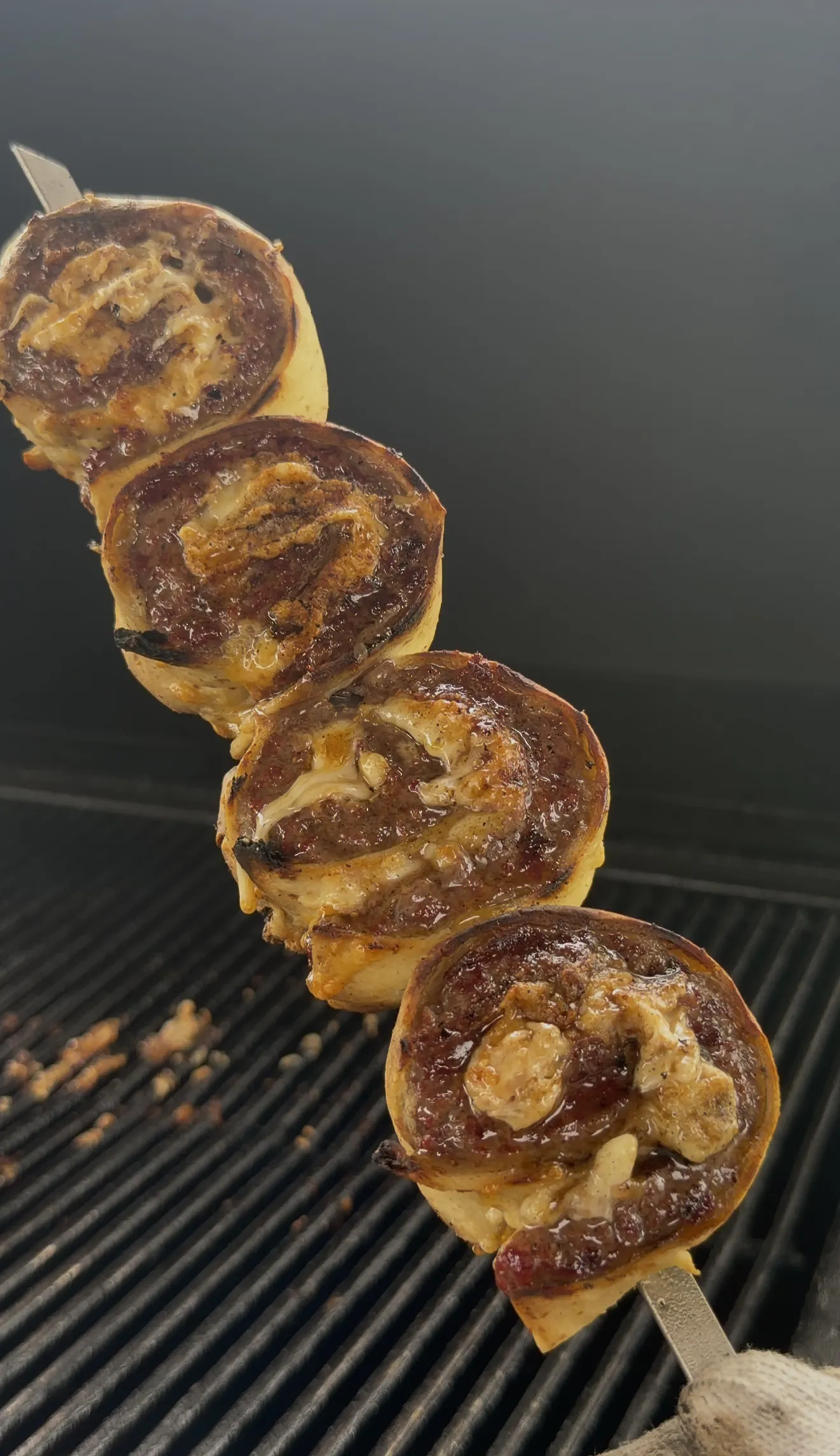 Grilled cowboy butter beef tortilla pinwheels stacked on a metal skewer over grill grates