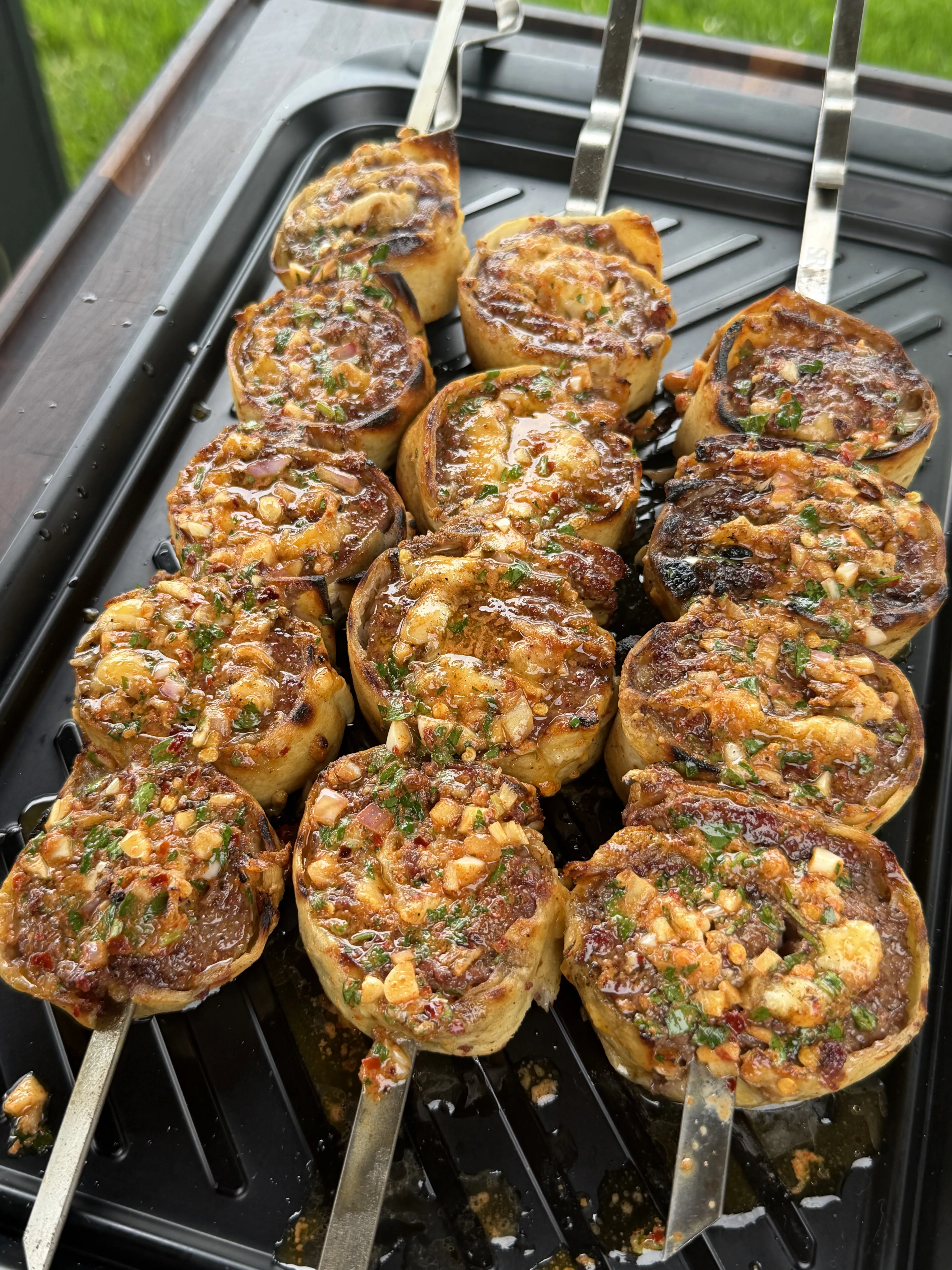 Grilled cowboy butter beef tortilla pinwheels on metal skewers topped with herbs, garlic, and chili flakes