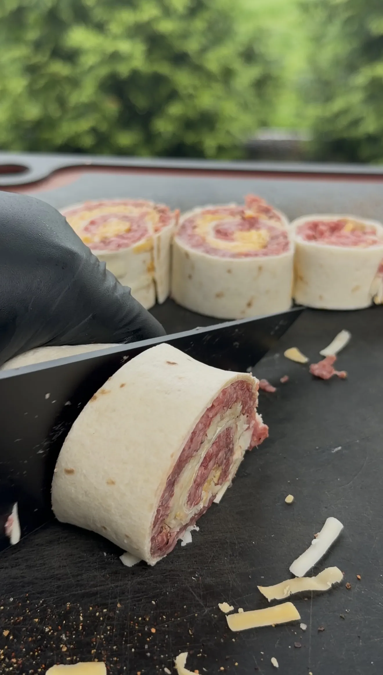 Beef tortilla pinwheels being sliced on a black cutting board showing layers of meat and cheese