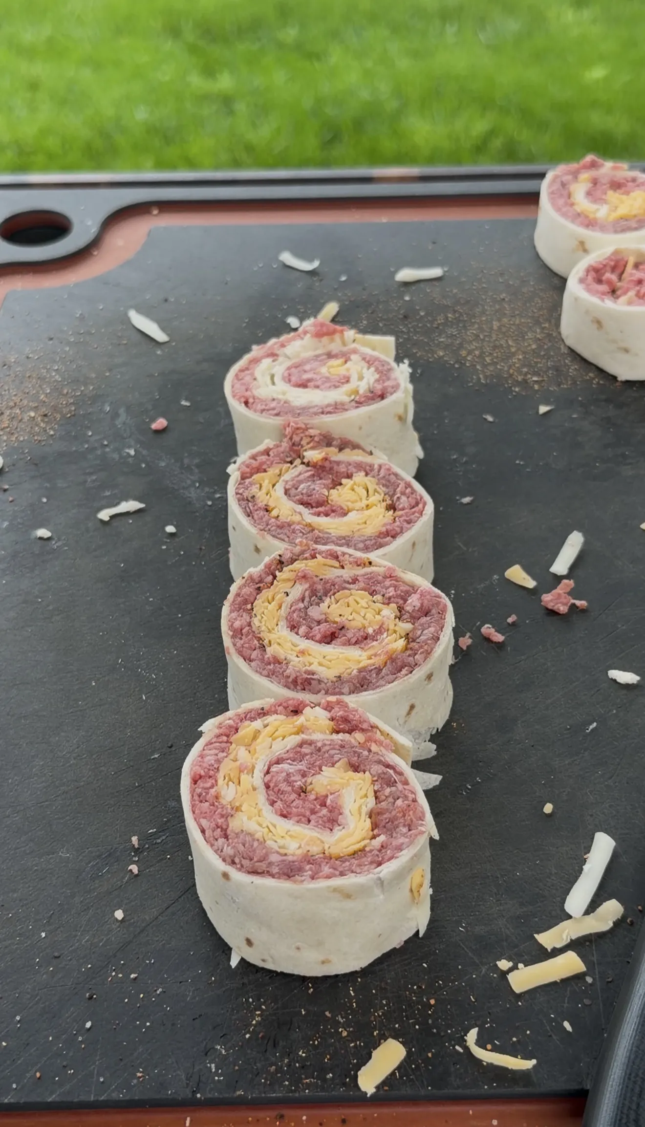 Raw ground beef and cheese tortilla pinwheels sliced and lined up on a griddle