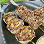 Golden brown jalapeño bacon beef pinwheels cooking in a black cast iron skillet, showing spiral layers