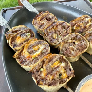 Golden brown jalapeño bacon beef pinwheels cooking in a black cast iron skillet, showing spiral layers