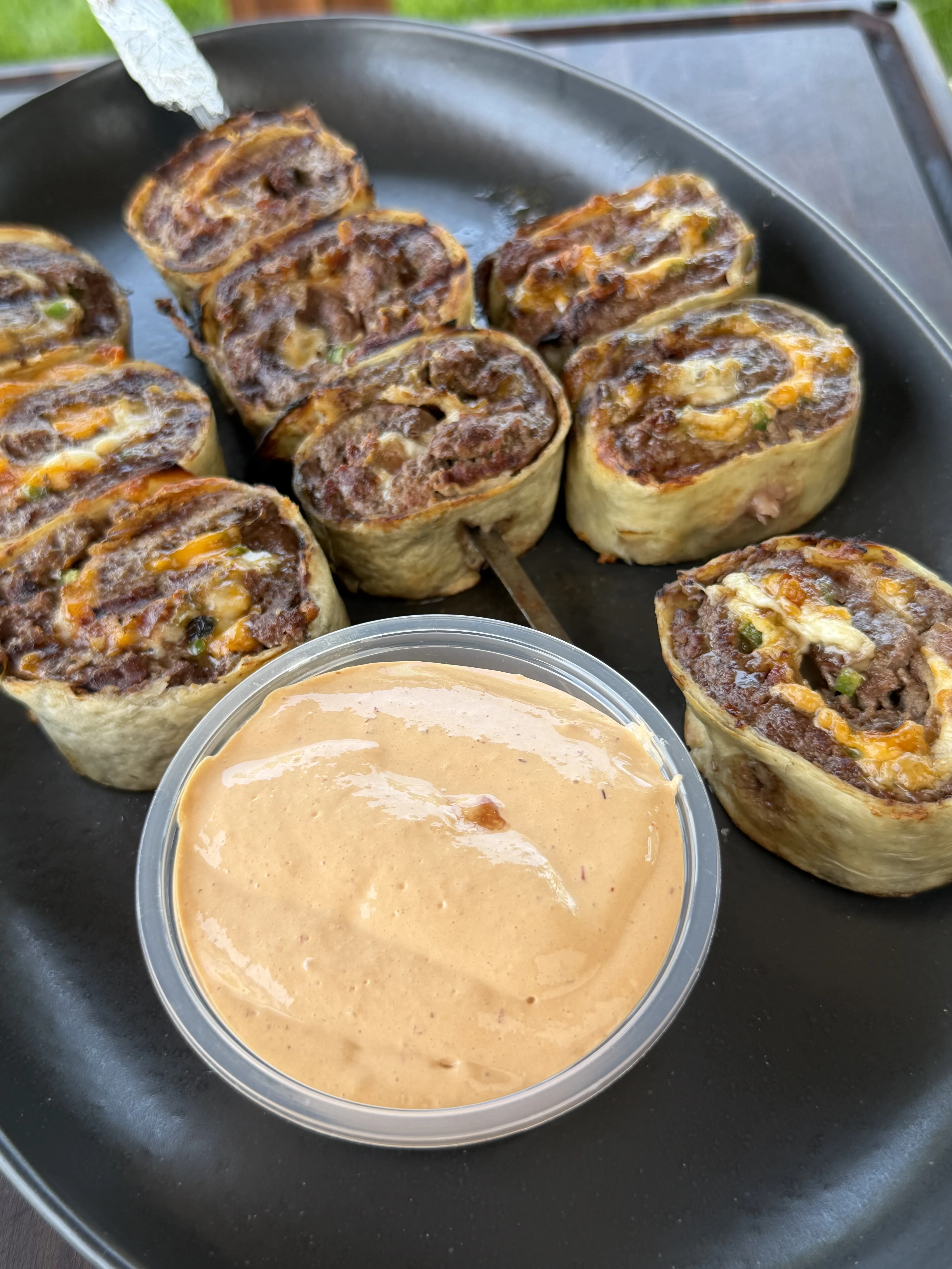 Golden crispy jalapeño bacon beef pinwheels arranged with chipotle crema dipping sauce
