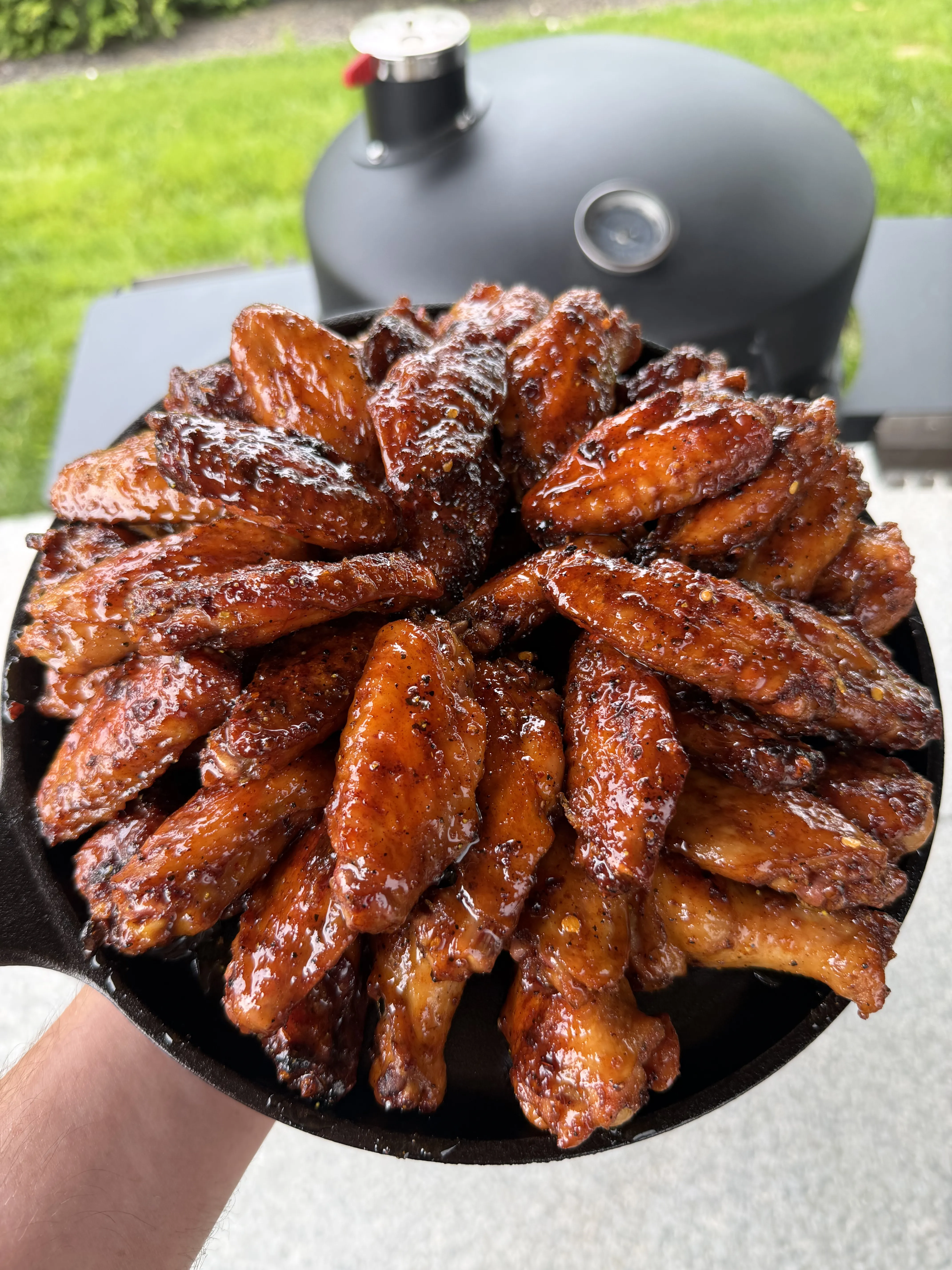 Golden glazed hot honey lemon pepper wings in a cast iron skillet with the smoker in the background