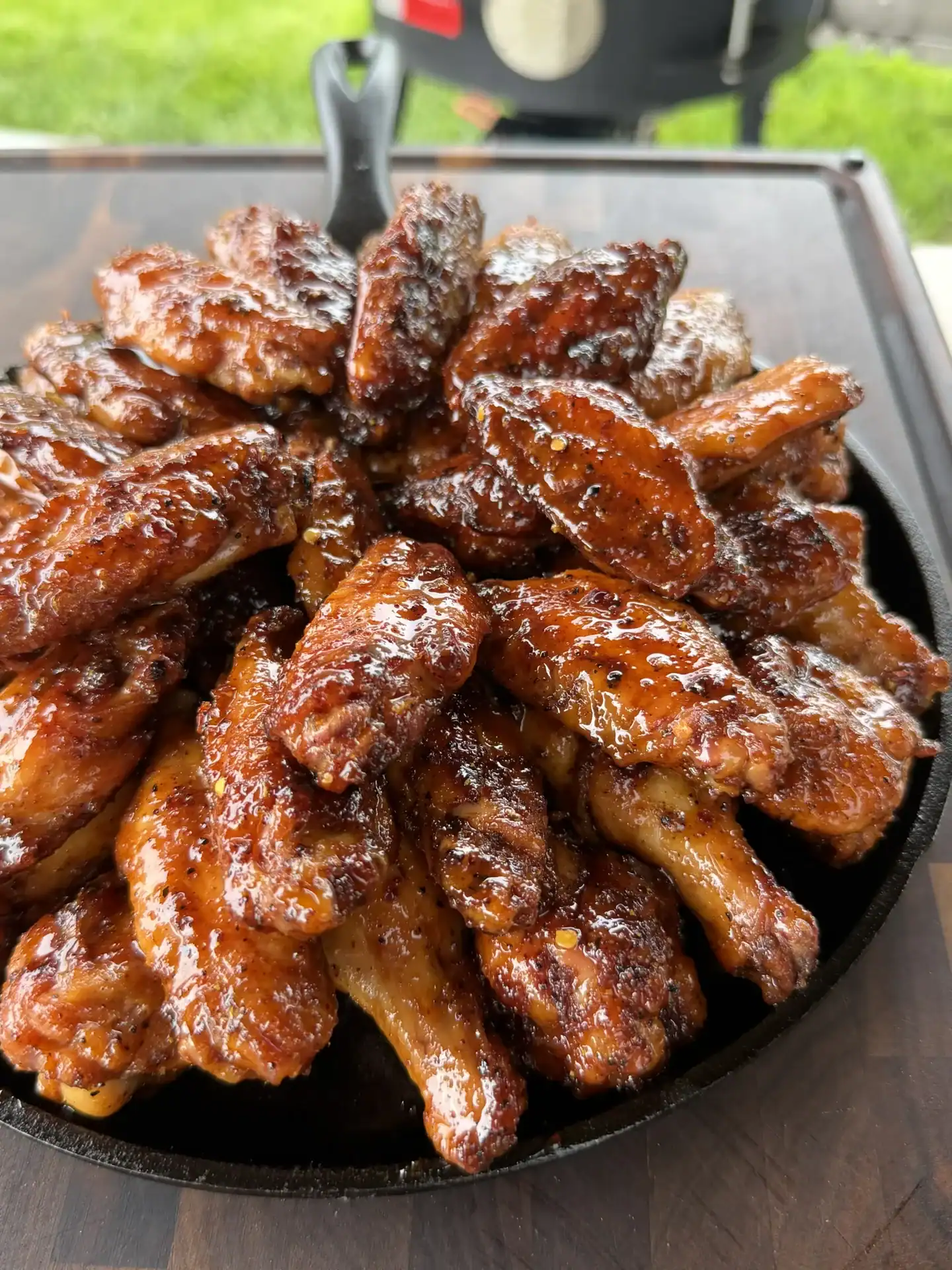 Glossy hot honey lemon pepper chicken wings with caramelized glaze arranged in a black cast iron skillet.