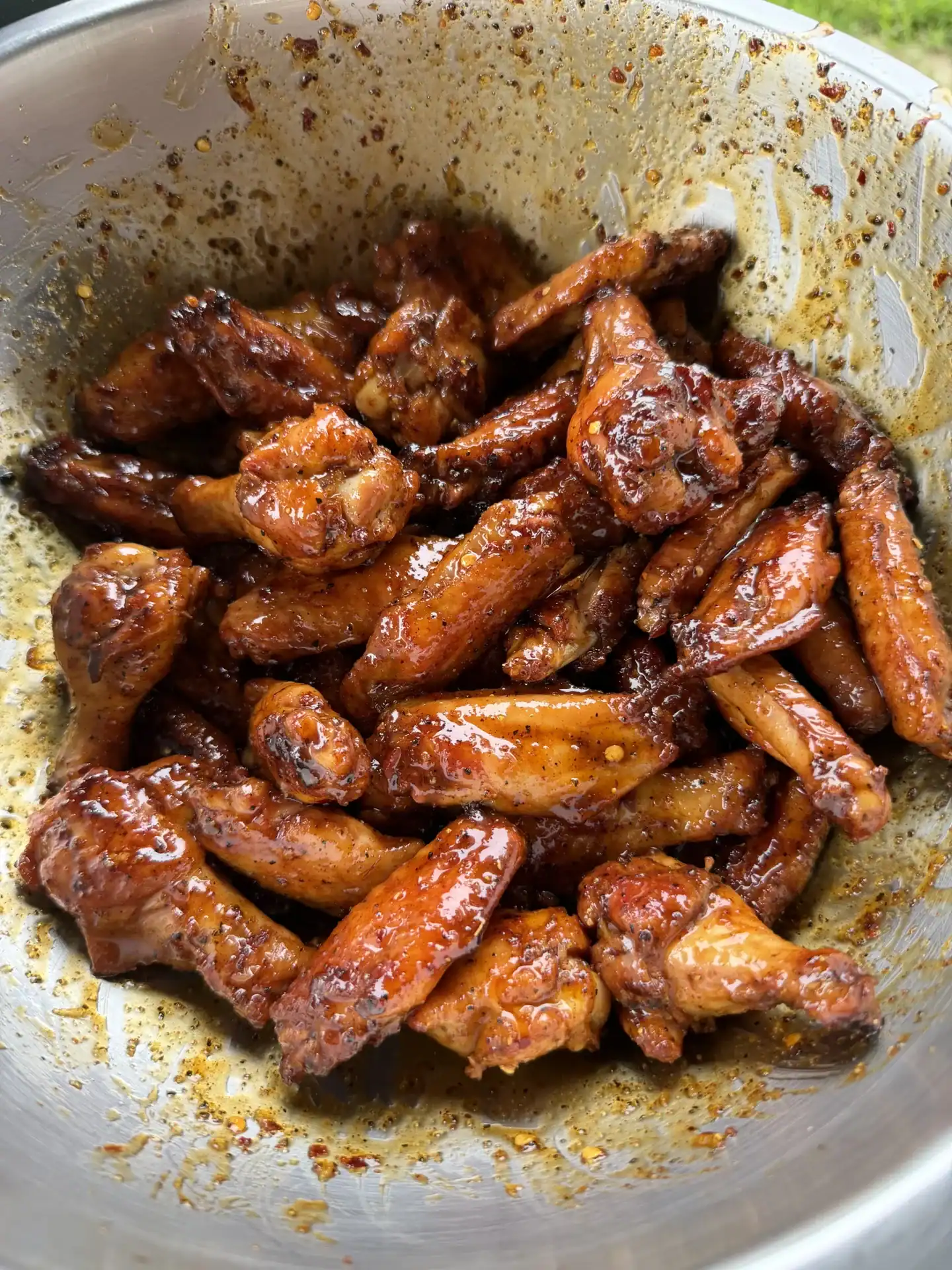 Glossy chicken wings with caramelized glaze and spices in a metal mixing bowl.