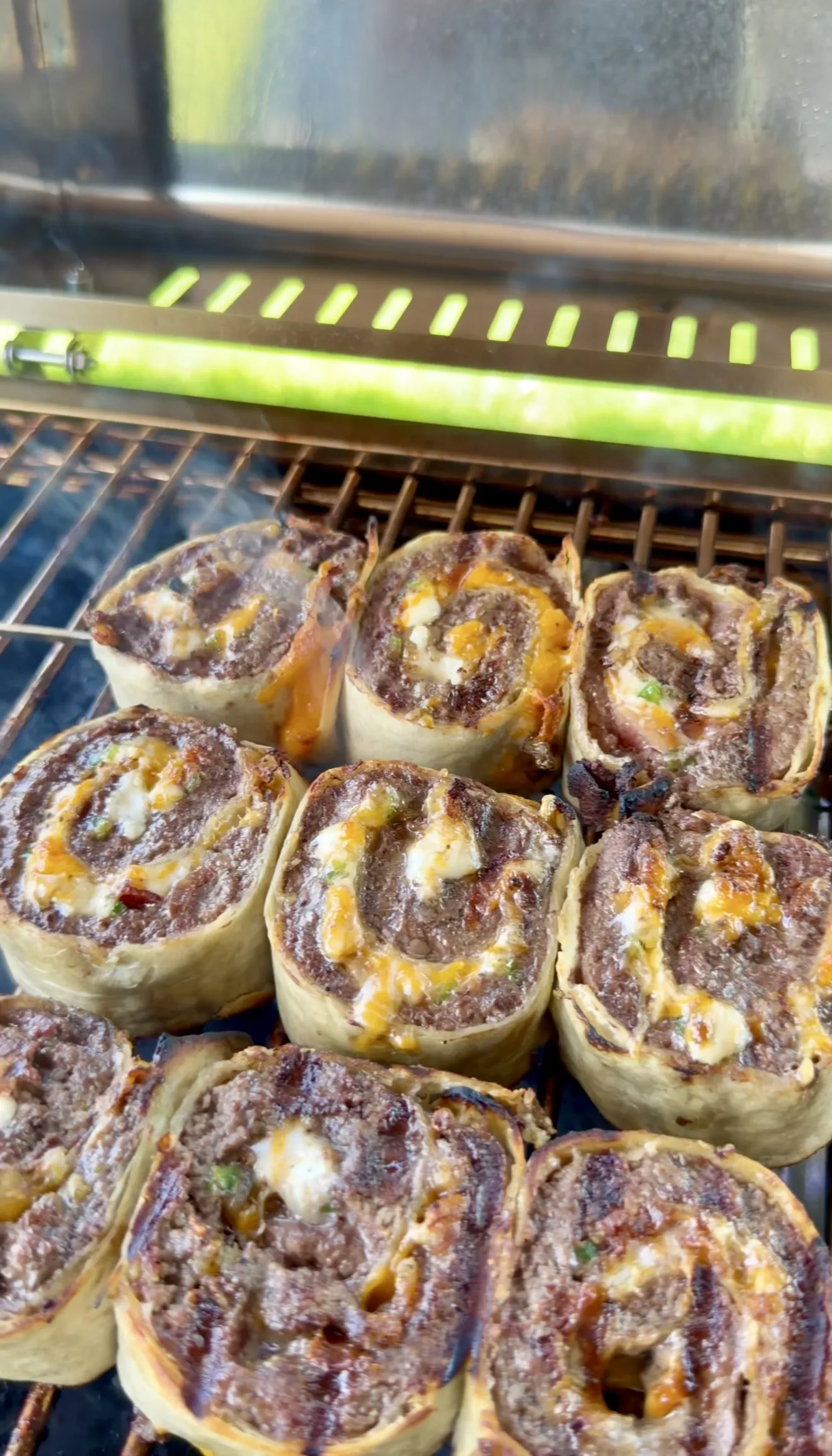 Crispy jalapeño bacon beef pinwheels cooking on a grill with melted cheese
